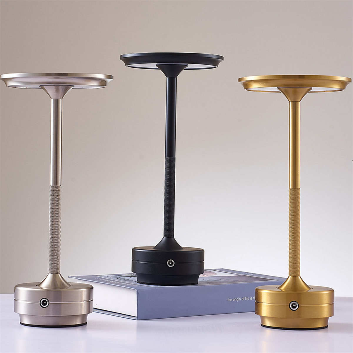 Drei moderne Tischlampen in Silber, Schwarz und Gold auf einer weißen Oberfläche.