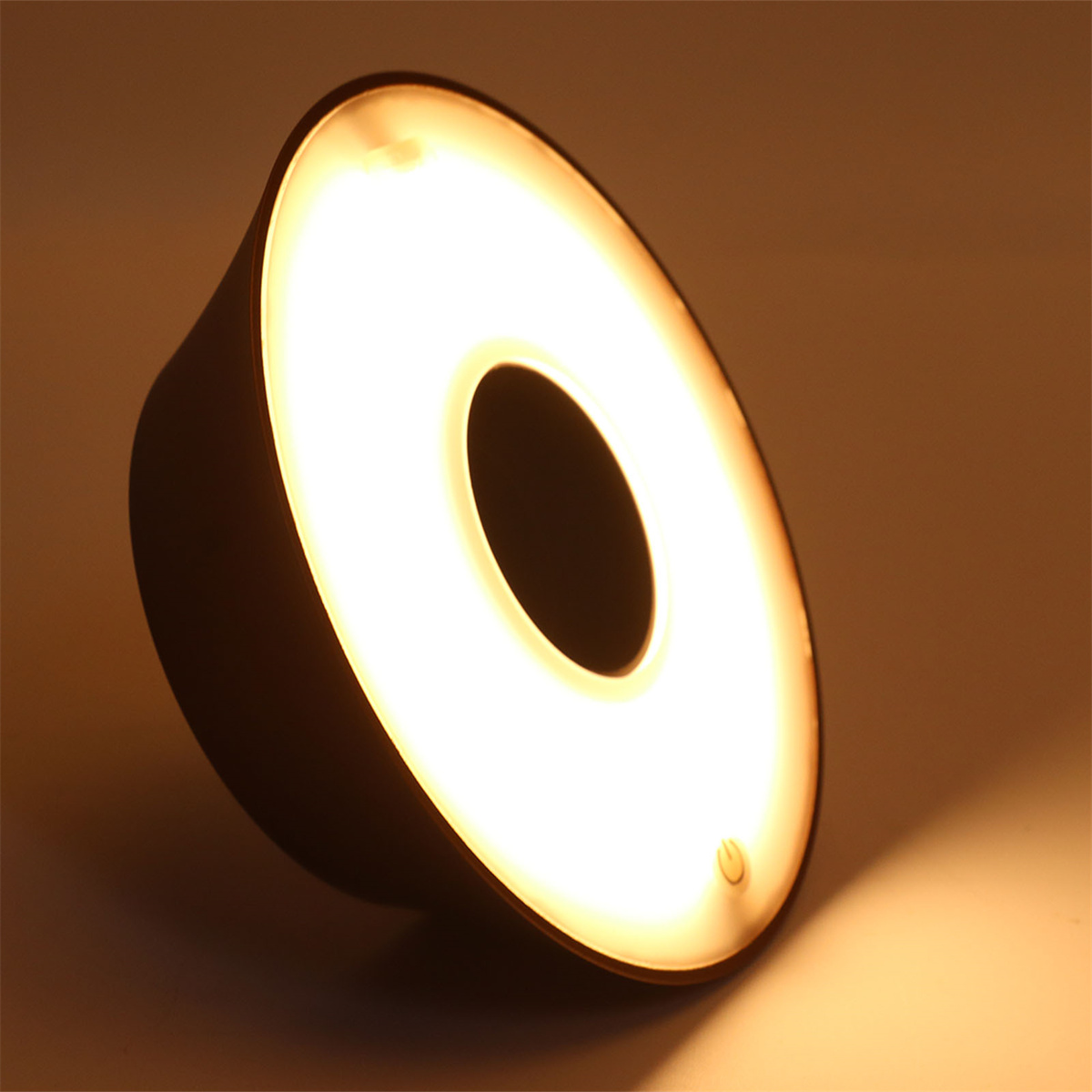 Eine runde, goldene Lampe mit einem zentralen Loch, die weiches Licht ausstrahlt.
