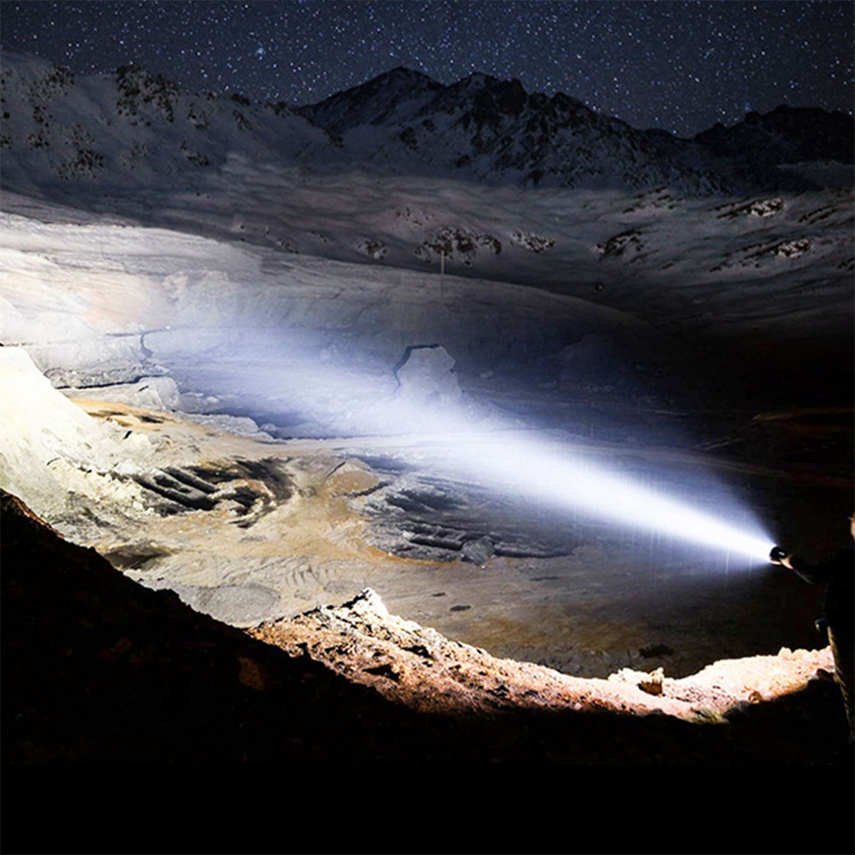 Person hält Taschenlampe, beleuchtet Höhle bei Nacht. Sternenhimmel sichtbar.