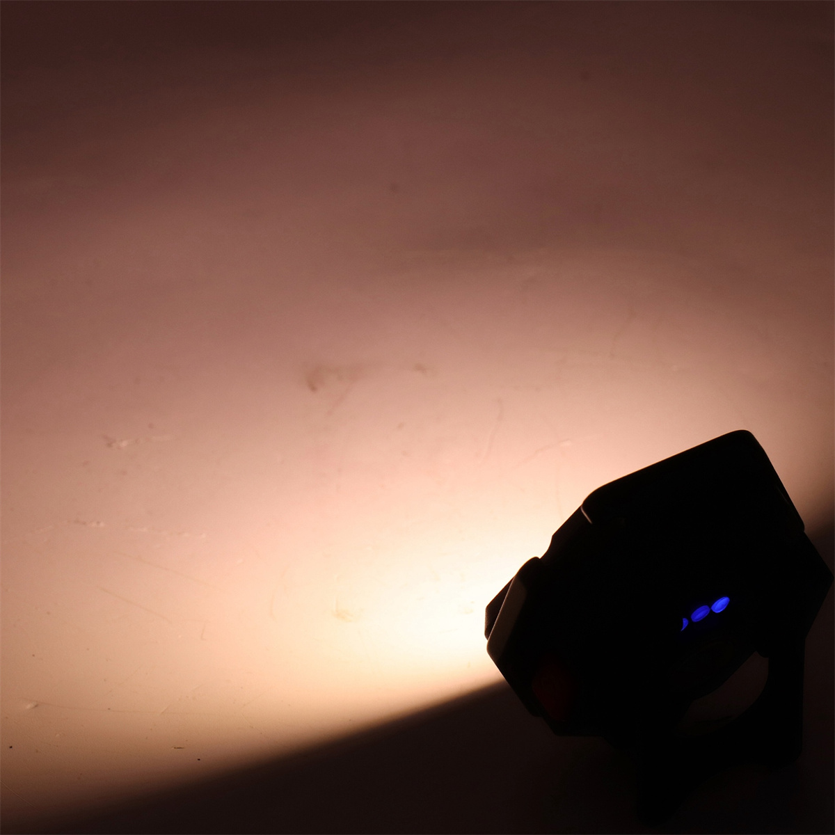 Ein Scheinwerfer, der eine Wand beleuchtet. Das Licht ist warm und der Scheinwerfer ist schwarz.