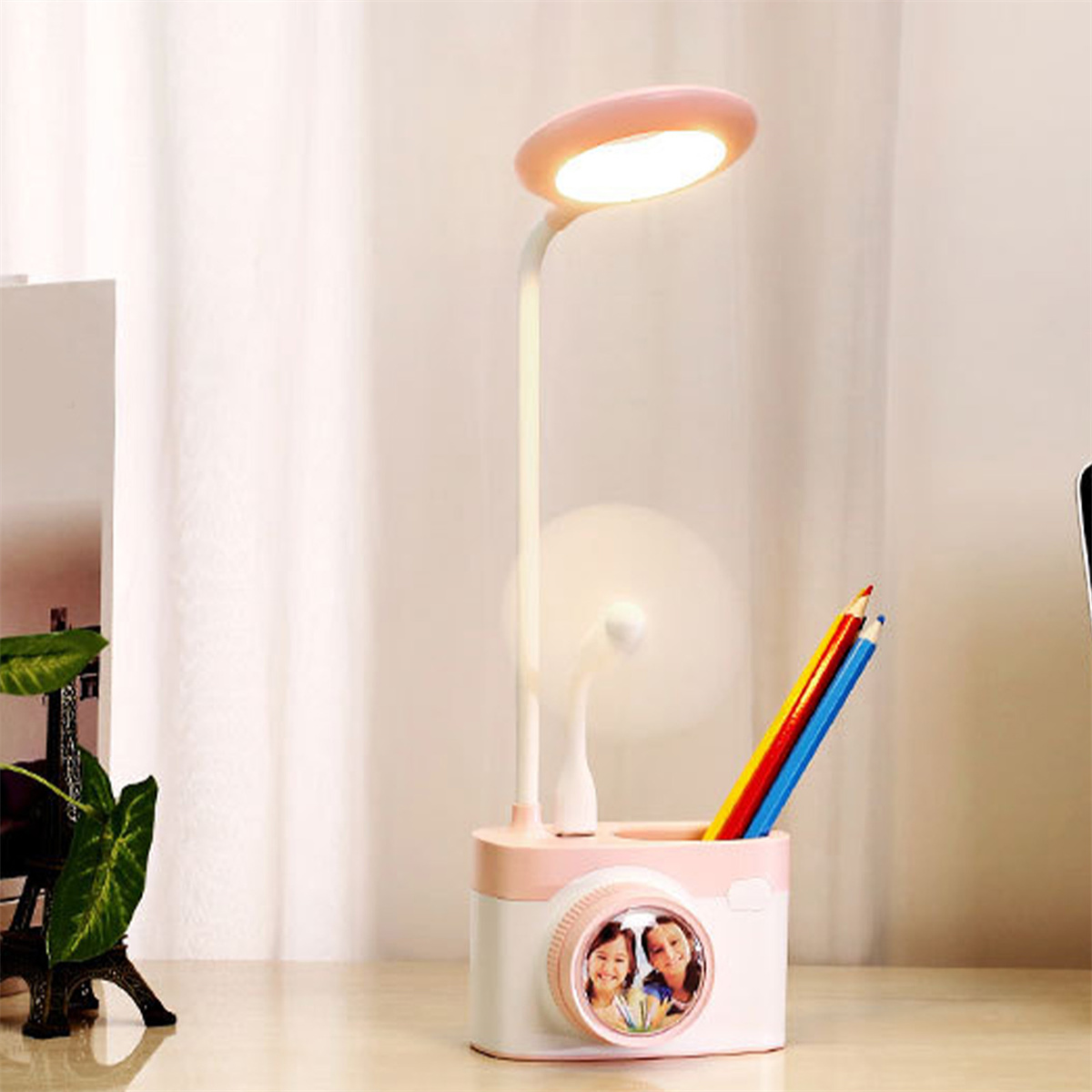 Eine rosa-weiße Schreibtischlampe mit Stifthalter und Stiften.