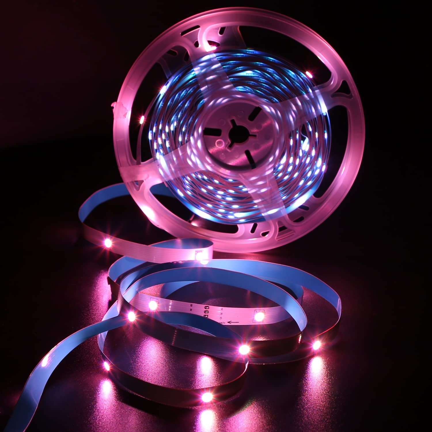 Un rotolo di strisce luminose a LED con un bagliore rosa e blu su una superficie scura.