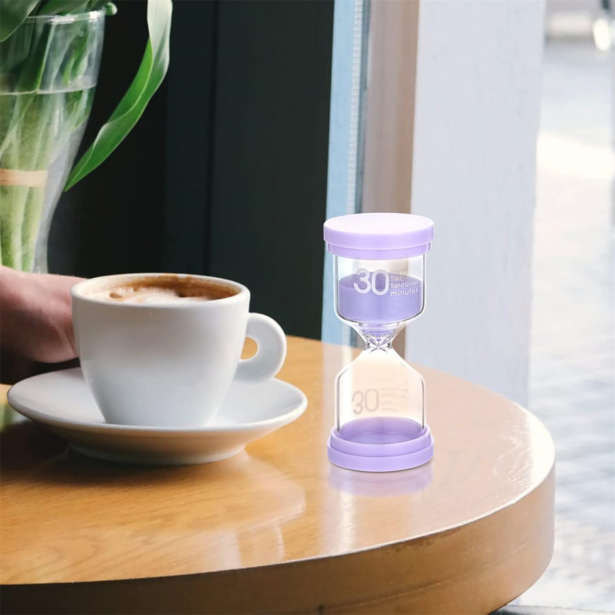 Stundenglas-Timer mit lila Sand. Eine Tasse Kaffee befindet sich links.