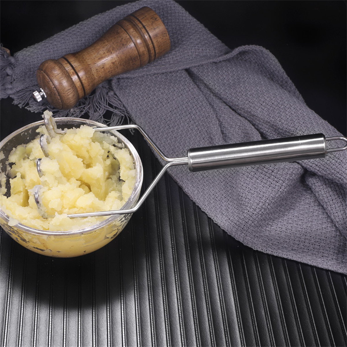 Kartoffelpüree in einer Schüssel mit einem Kartoffelstampfer und einer hölzernen Pfeffermühle.