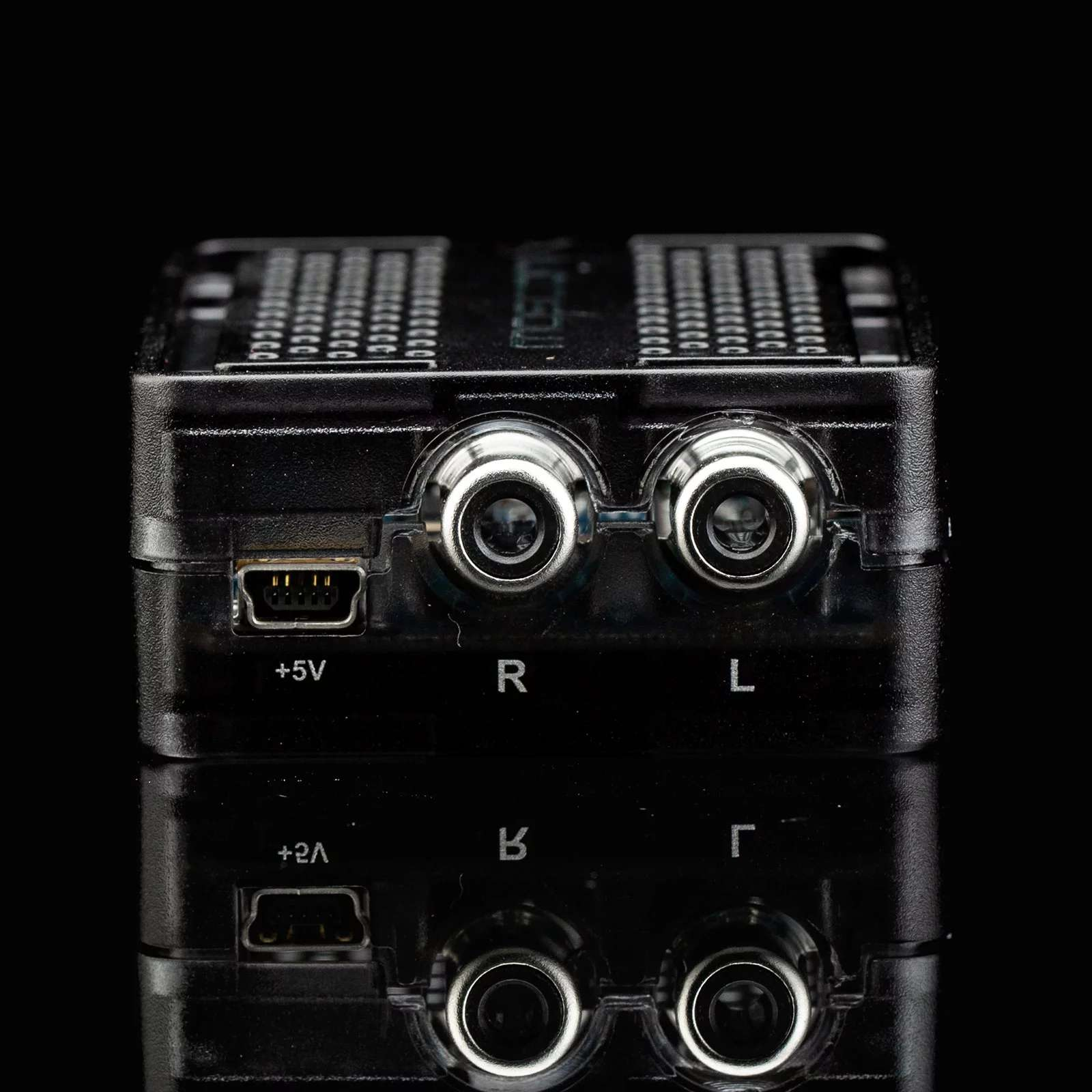 Ein schwarzes, rechteckiges Gerät mit den Anschlüssen +5V, R, L und +2A auf einer reflektierenden Oberfläche.