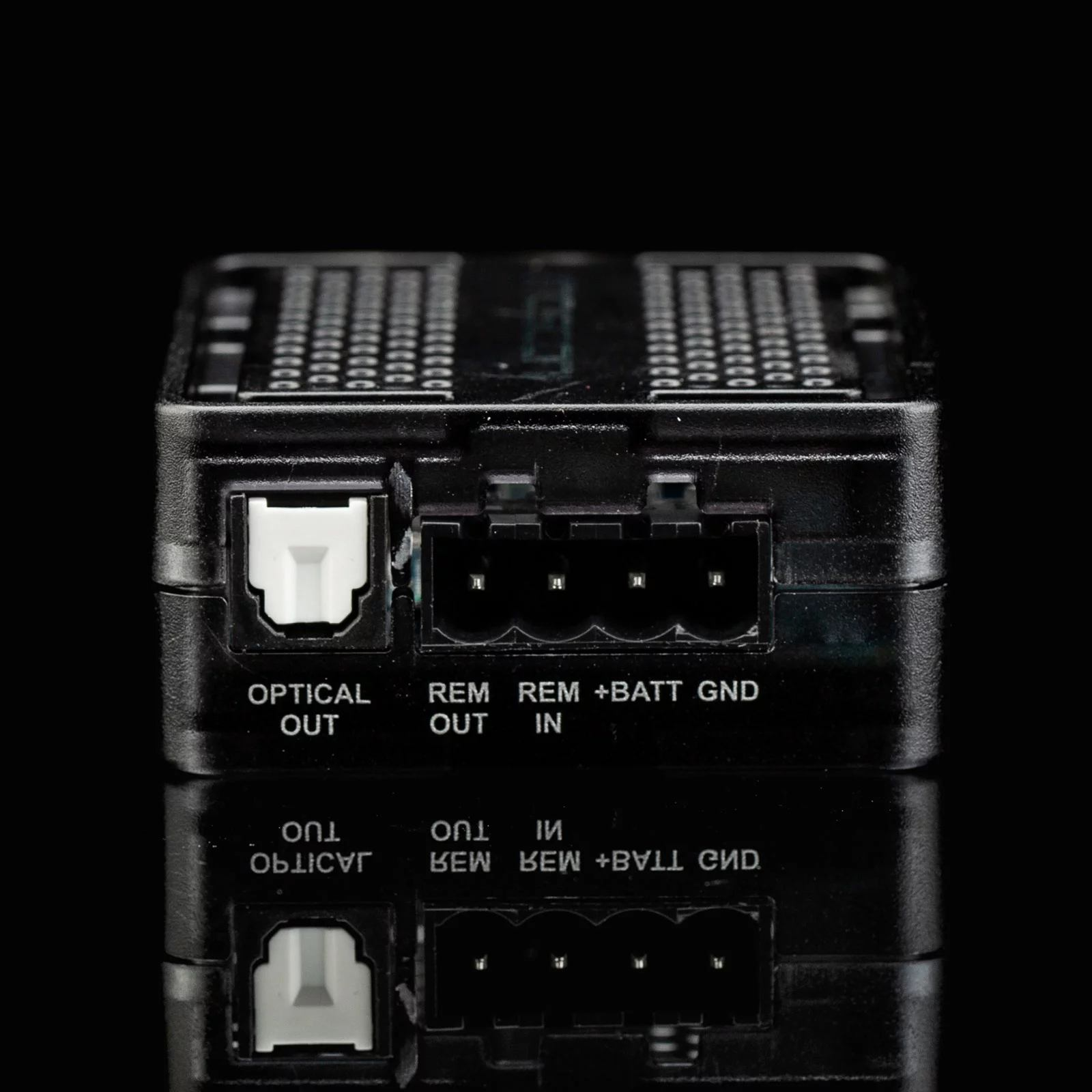 Schwarze Box mit Anschlüssen und Beschriftungen, auf reflektierender schwarzer Oberfläche.