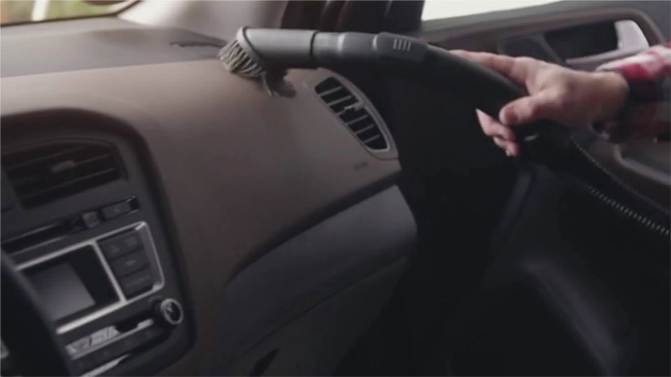 Una persona aspirando el salpicadero de un coche con una aspiradora de mano.