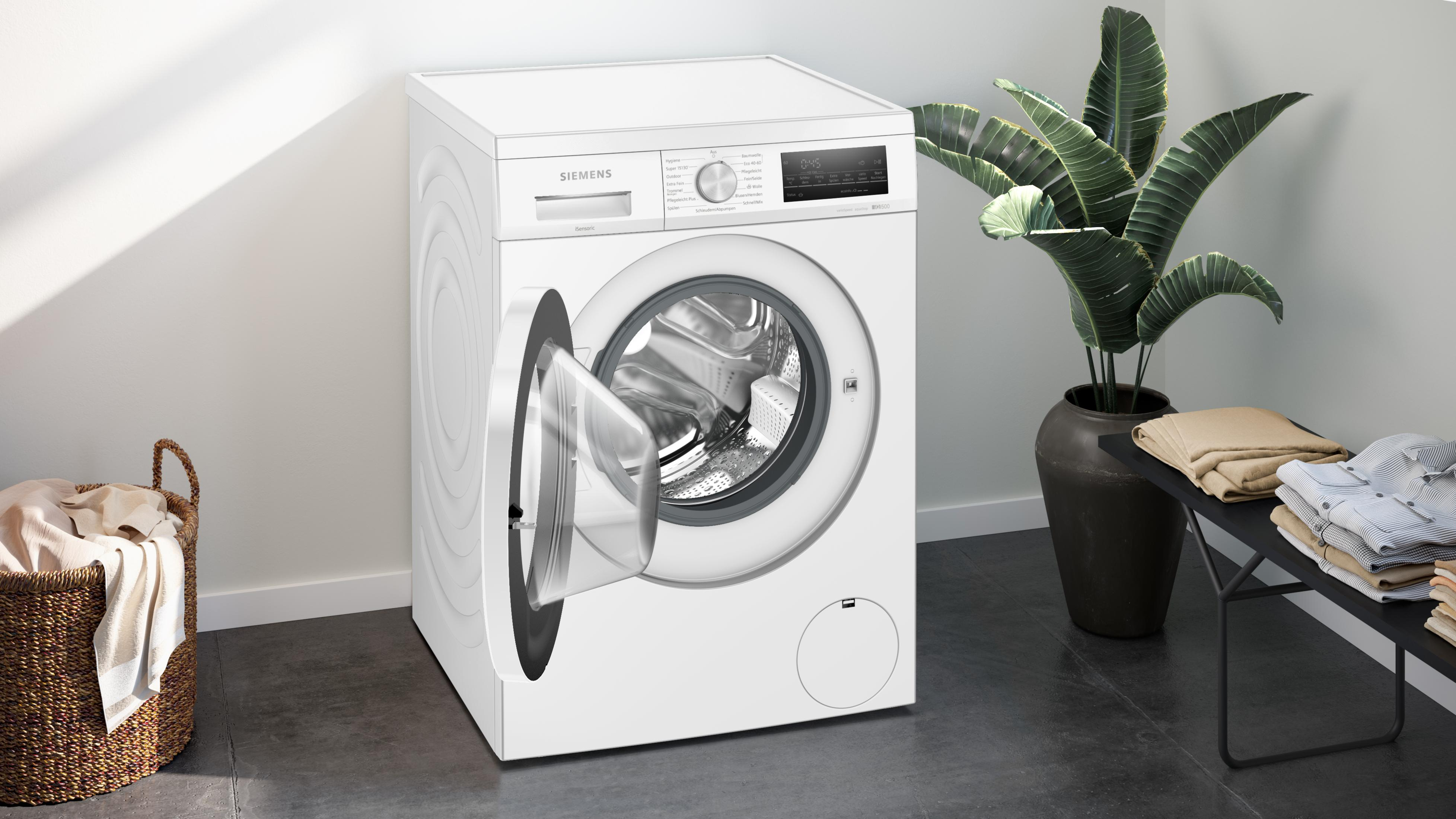 Weiße Siemens Waschmaschine mit offener Tür. Wäschekorb, Bank und Pflanze daneben.