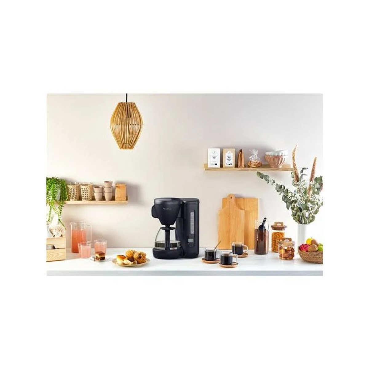 A coffee maker, cups, pastries, and cutting boards on a counter in a kitchen.