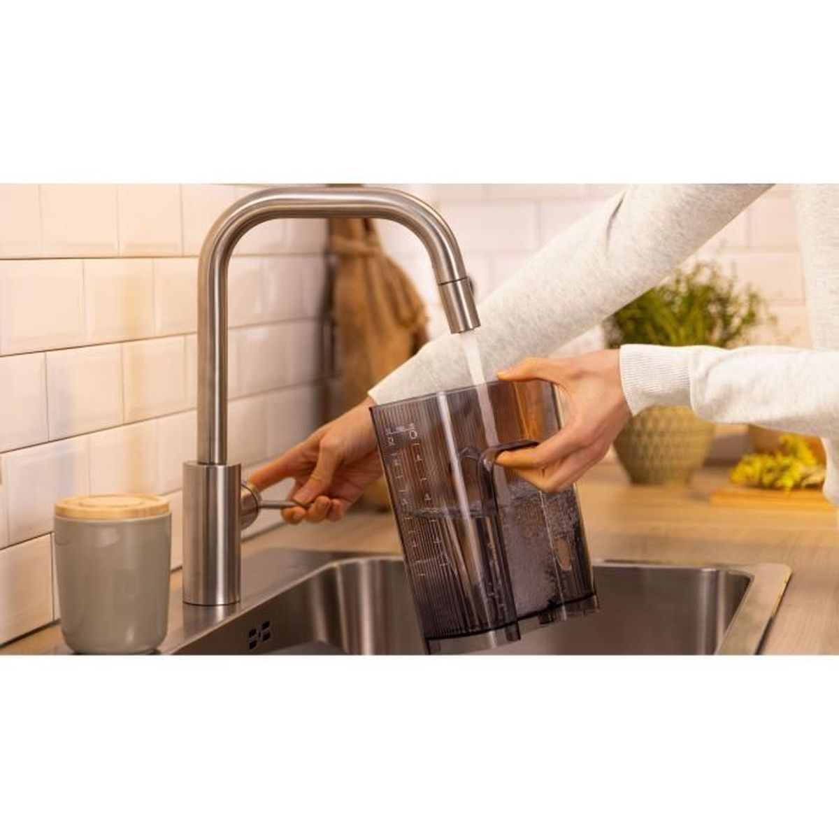 Osoba napełnia przezroczysty pojemnik wodą z kranu kuchennego.