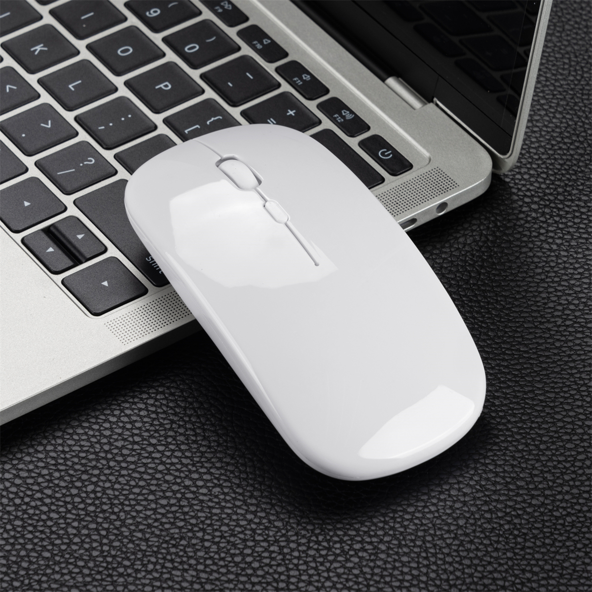 Weiße kabellose Maus auf schwarzer Oberfläche in der Nähe einer Laptop-Tastatur. Die Maus ist leicht angewinkelt.