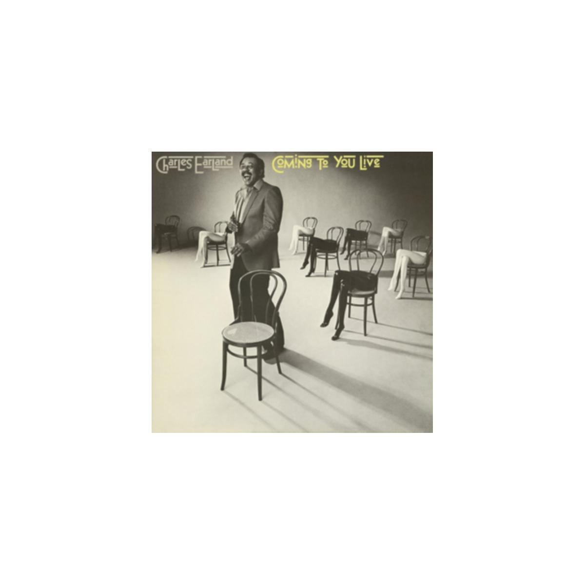 Pochette de l'album Coming to You Live. Homme en costume debout près d'une chaise.