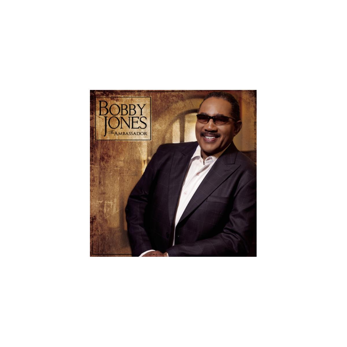 Bobby Jones, de ambassadeur, lacht in een pak met een bruine achtergrond.