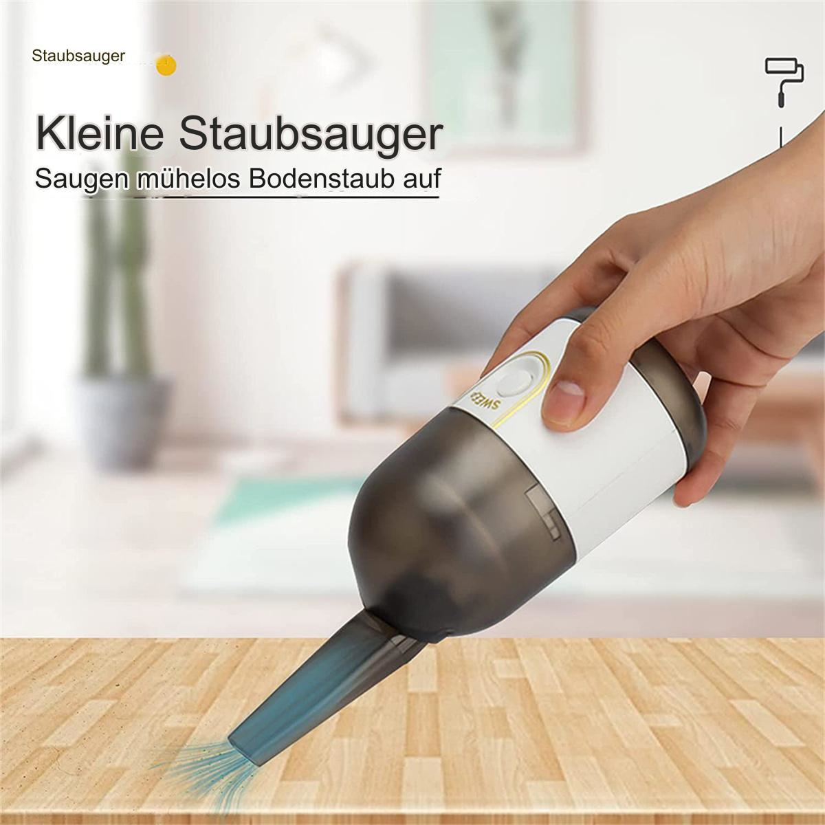 Hand hält einen kleinen weißen und grauen Staubsauger. Er reinigt eine Holzoberfläche.