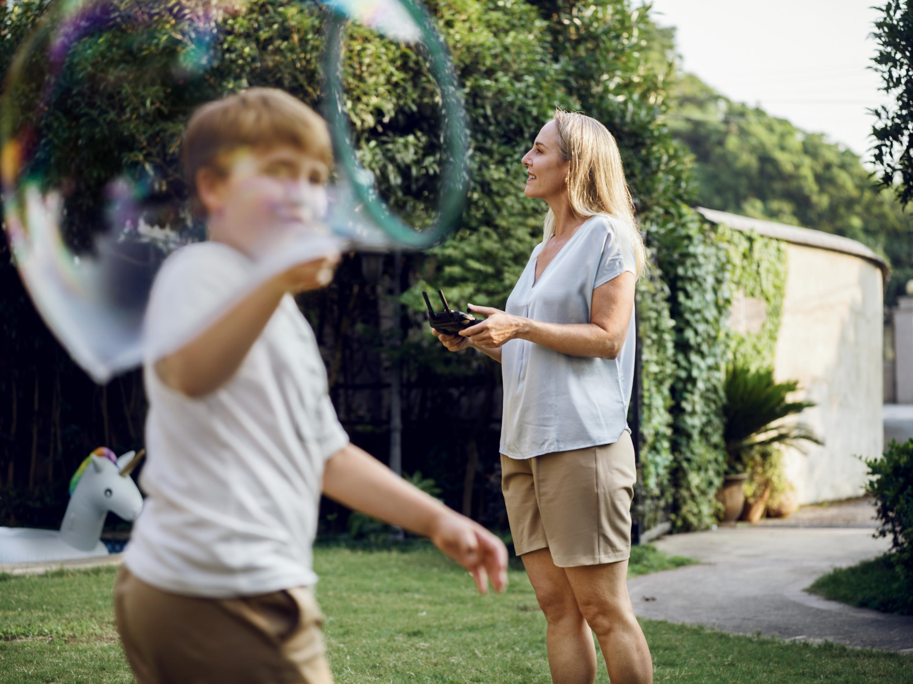 Eine Frau mit Fernbedienung beobachtet einen Jungen, der im Garten eine Blase macht.