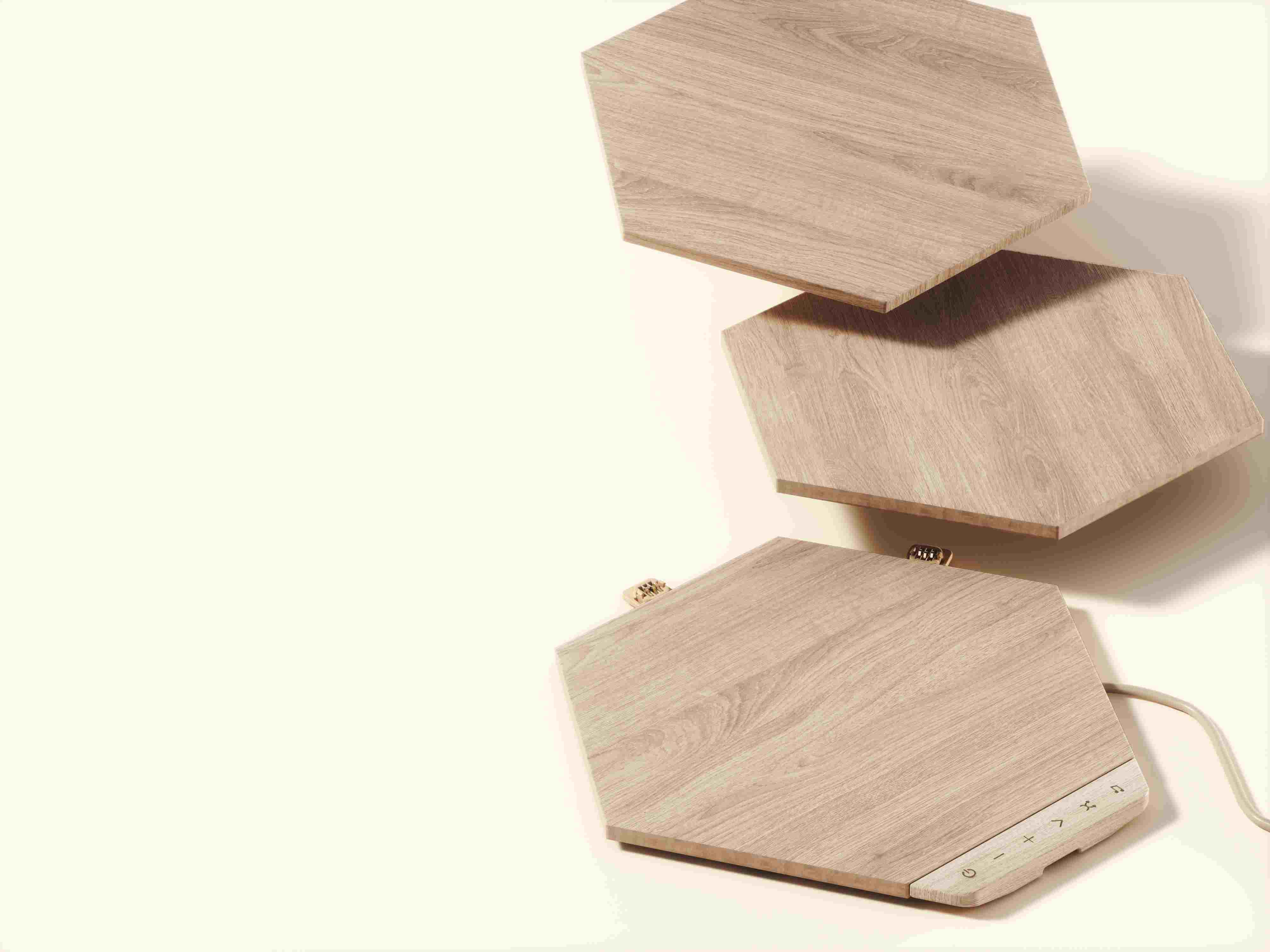 Drei sechseckige Lautsprecher aus Holz, einer mit Bedienelementen, vor weißem Hintergrund.