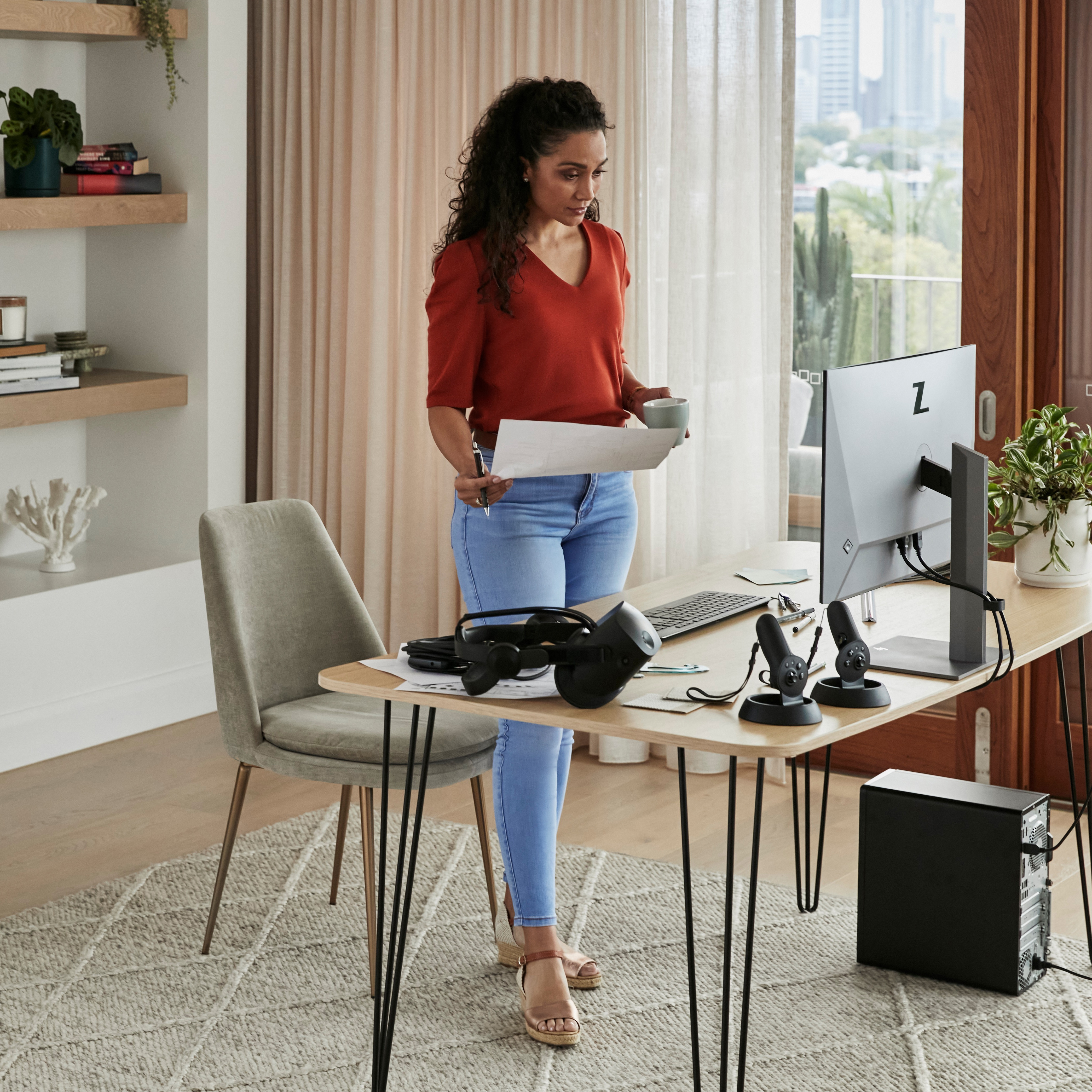 Donna a una scrivania con un monitor, che tiene in mano dei fogli, con un computer e un visore VR.