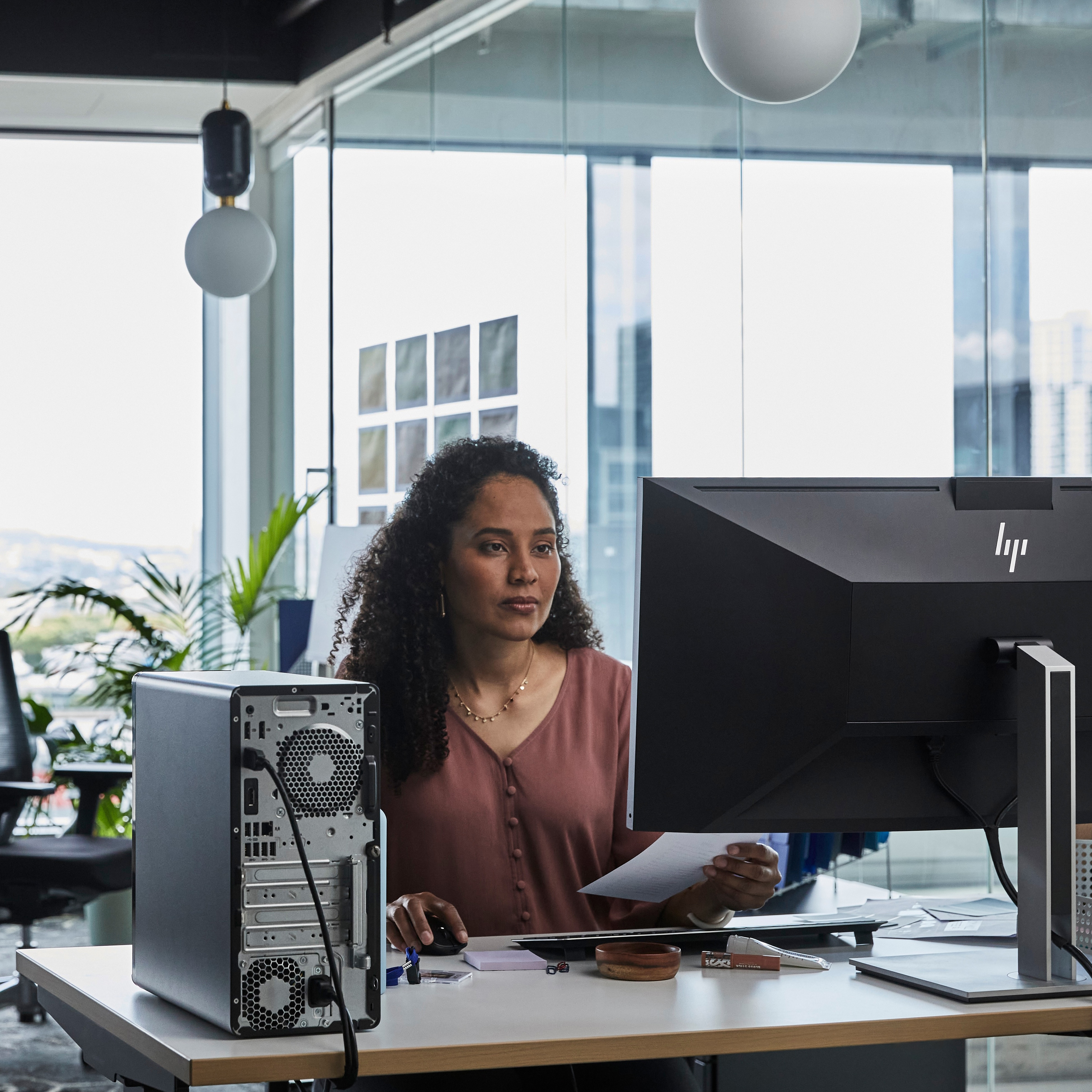 Frau arbeitet am Schreibtisch, schaut auf einen Computerbildschirm und hält Papier.