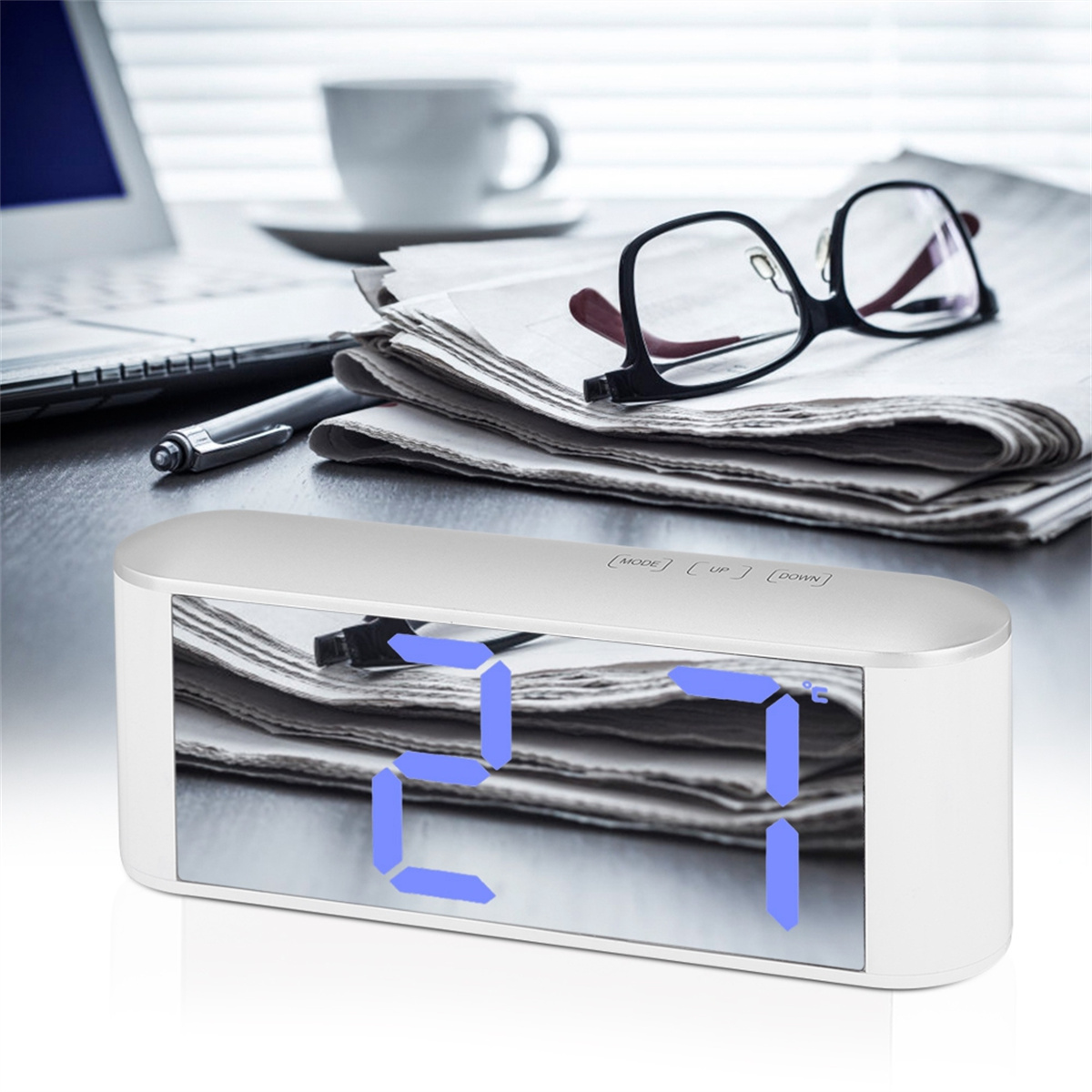 Weiße Uhr zeigt 27 Grad. Brille und Zeitungen liegen auf dem Schreibtisch. Eine Kaffeetasse im Hintergrund.