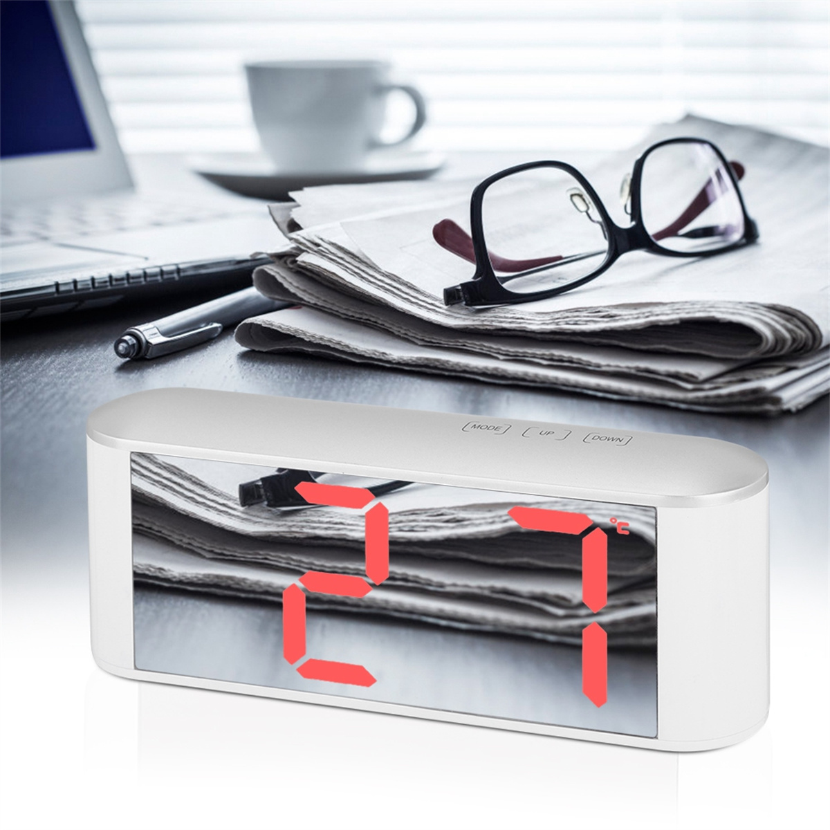 Ein digitaler Wecker auf einem Schreibtisch mit Zeitungen, Brille und Kaffeetasse.