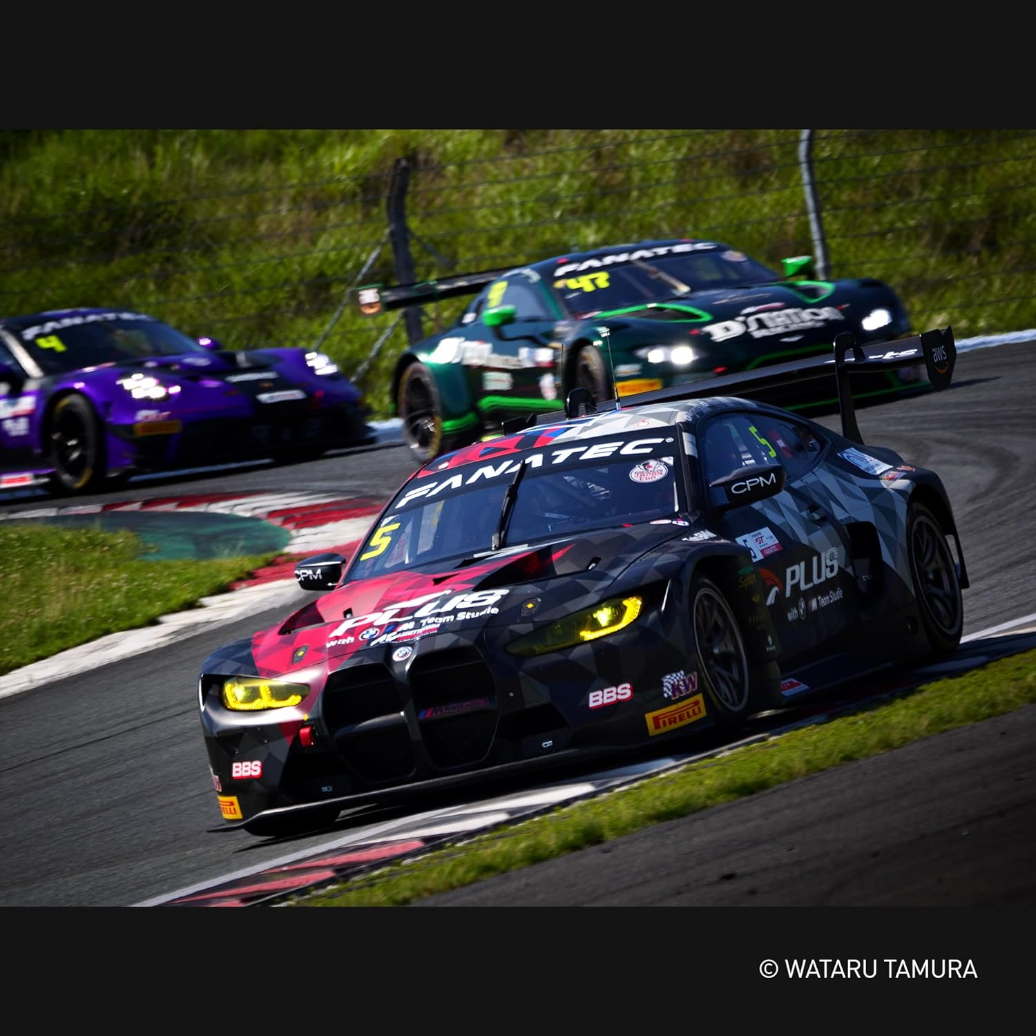 Samochody wyścigowe ścigają się na torze. Samochody są czarne, zielone i fioletowe.