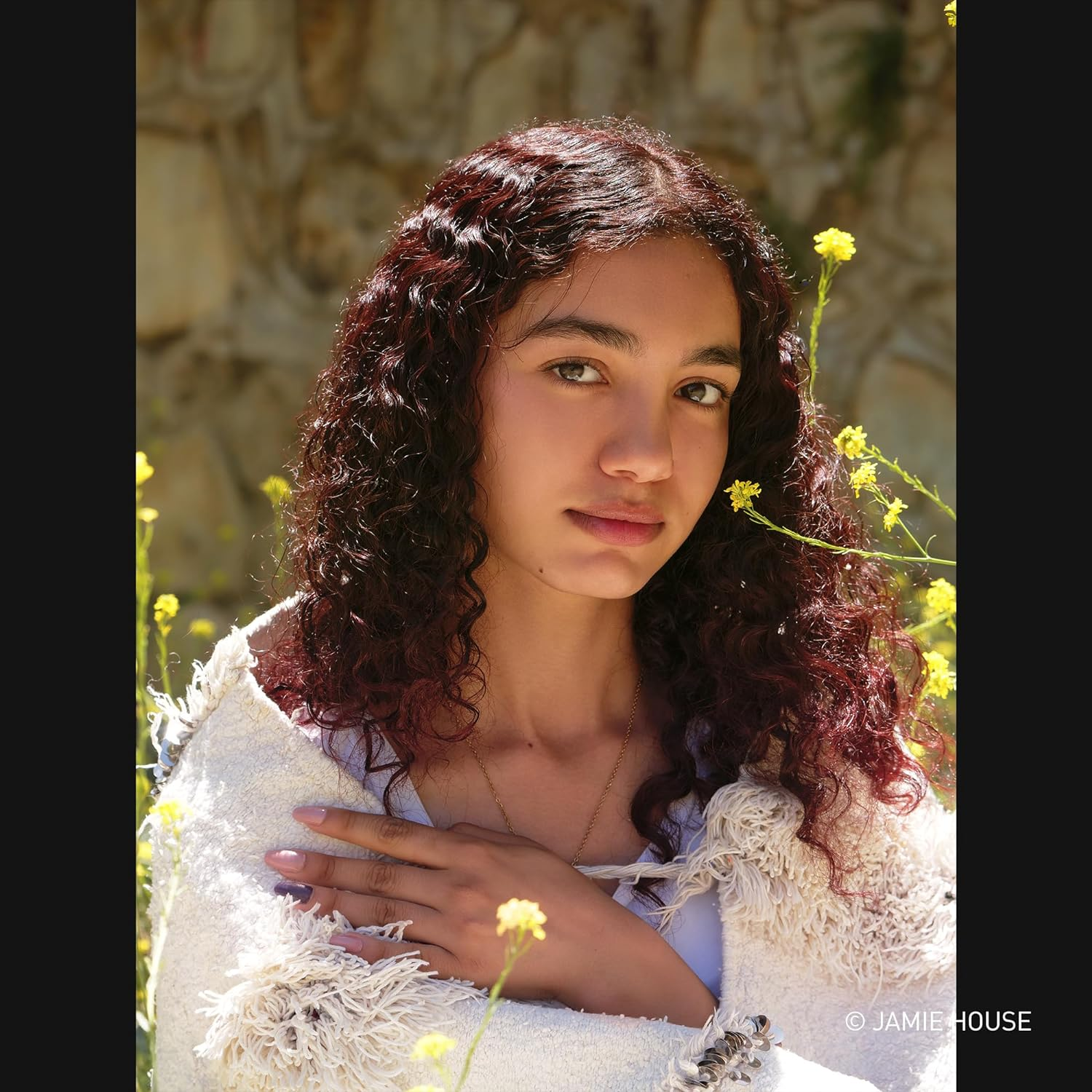 Portret młodej kobiety z kręconymi kasztanowymi włosami, w kremowym otulaczu, z żółtymi kwiatami z boku.