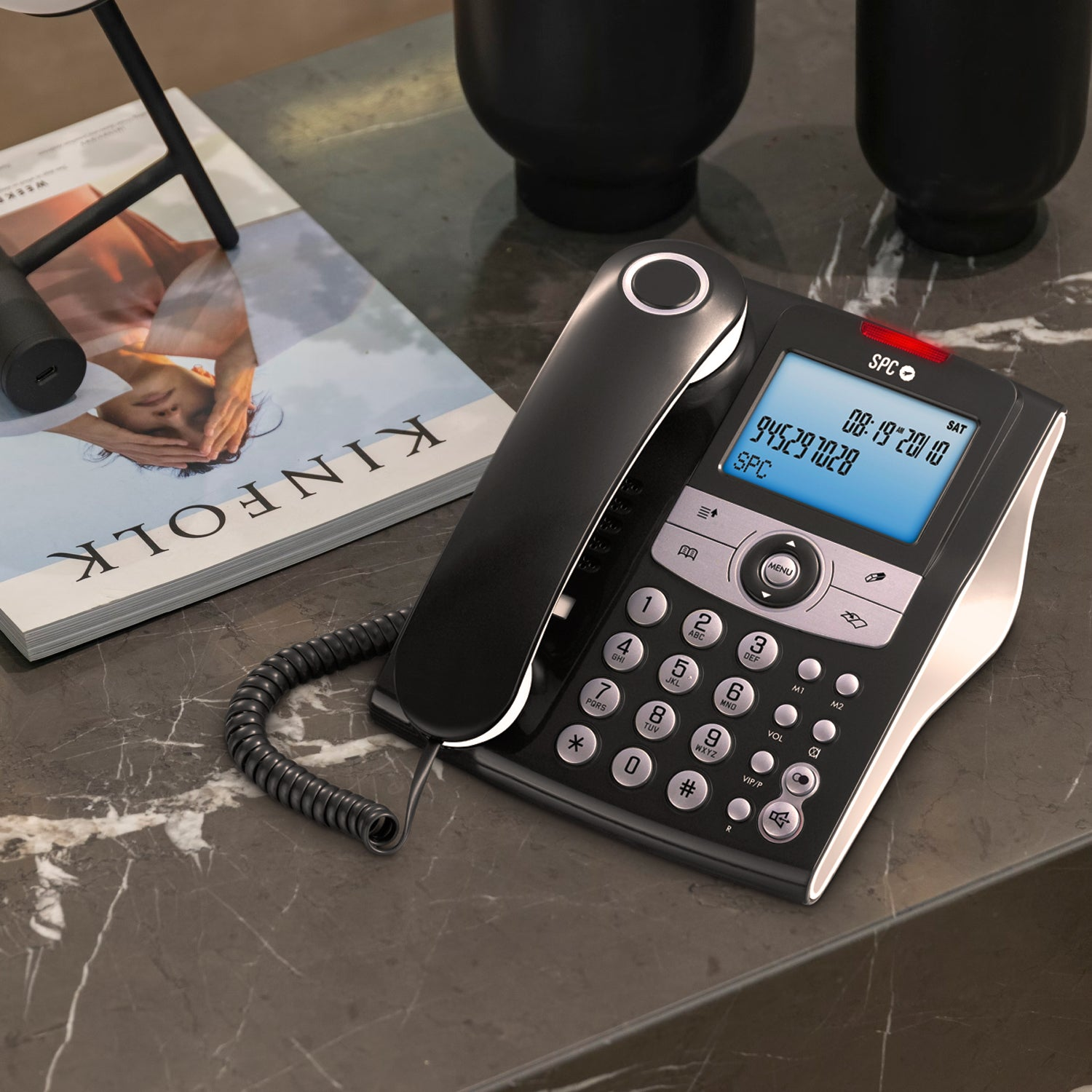 Telefono nero con display su tavolo in marmo, con rivista e decorazioni.