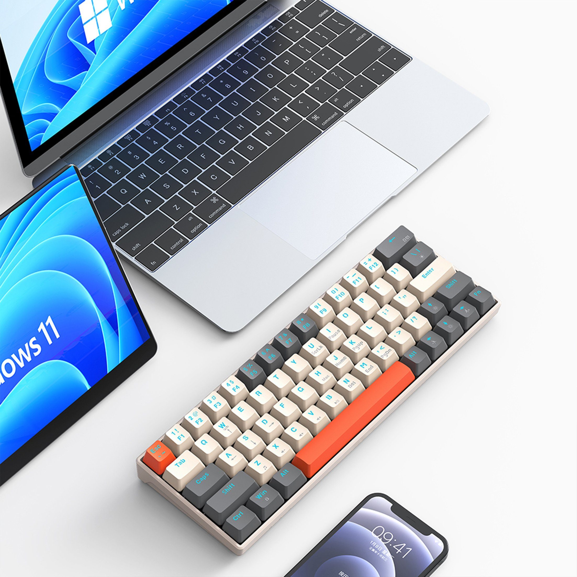 Eine Tastatur, ein Laptop, ein Tablet und ein Telefon. Die Tastatur ist grau, weiß und orange. Der Laptop ist offen.