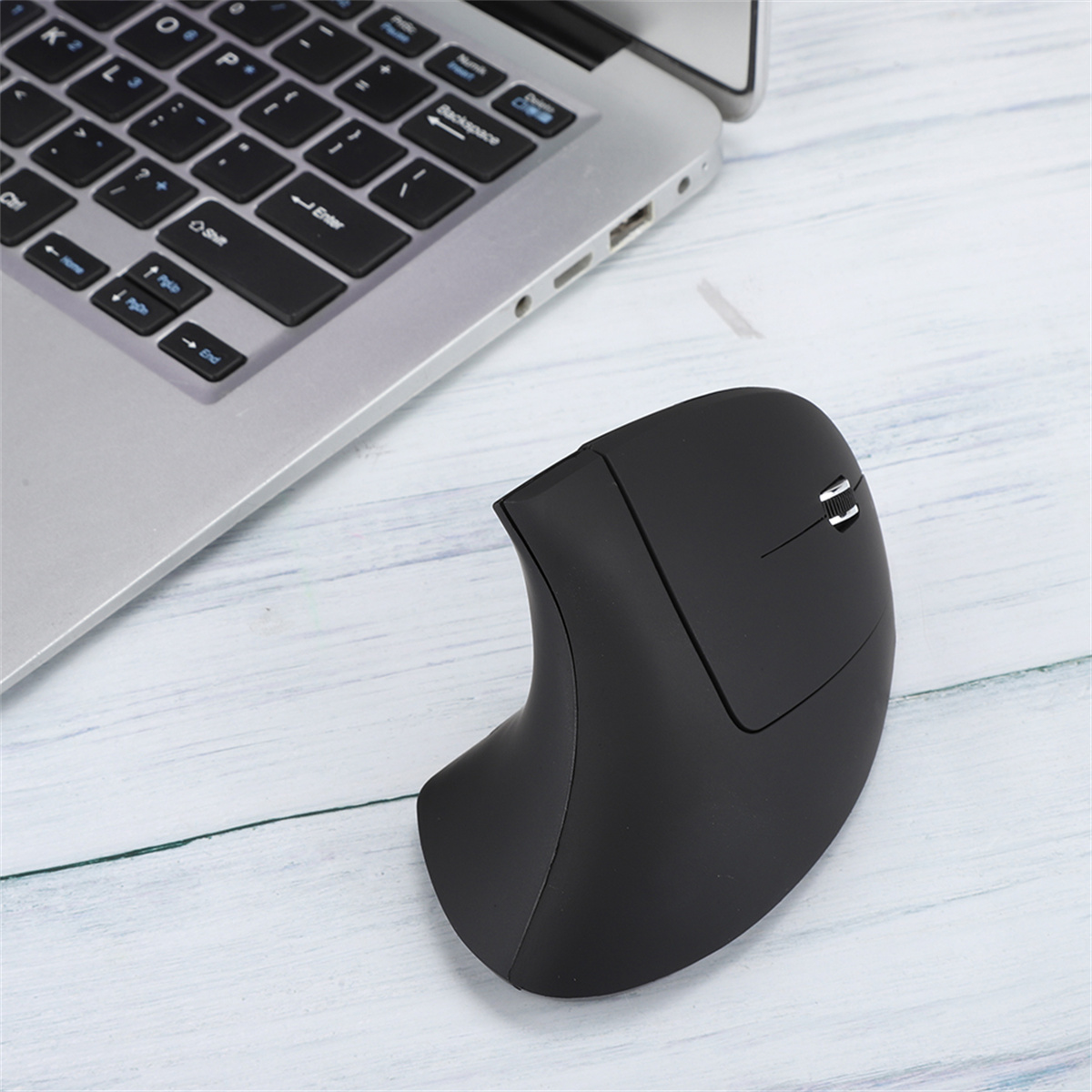 Schwarze ergonomische vertikale Maus neben Laptop-Tastatur auf hellem Holz. Weißer und grauer Hintergrund.