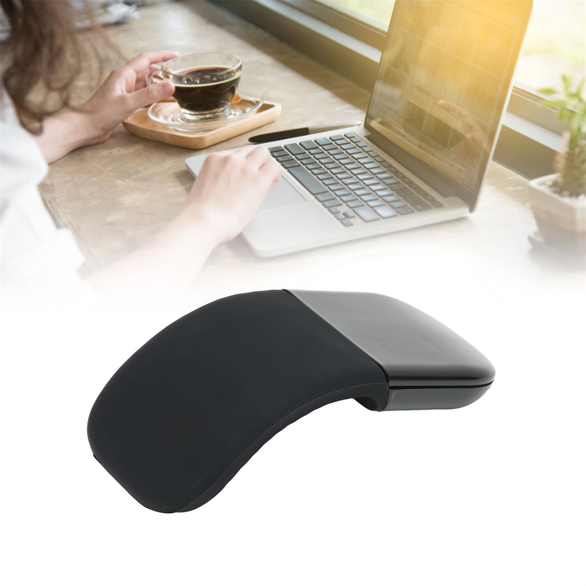 Schwarze Maus auf einem Tisch, im Hintergrund eine Person, die einen Laptop benutzt und eine Kaffeetasse hält.
