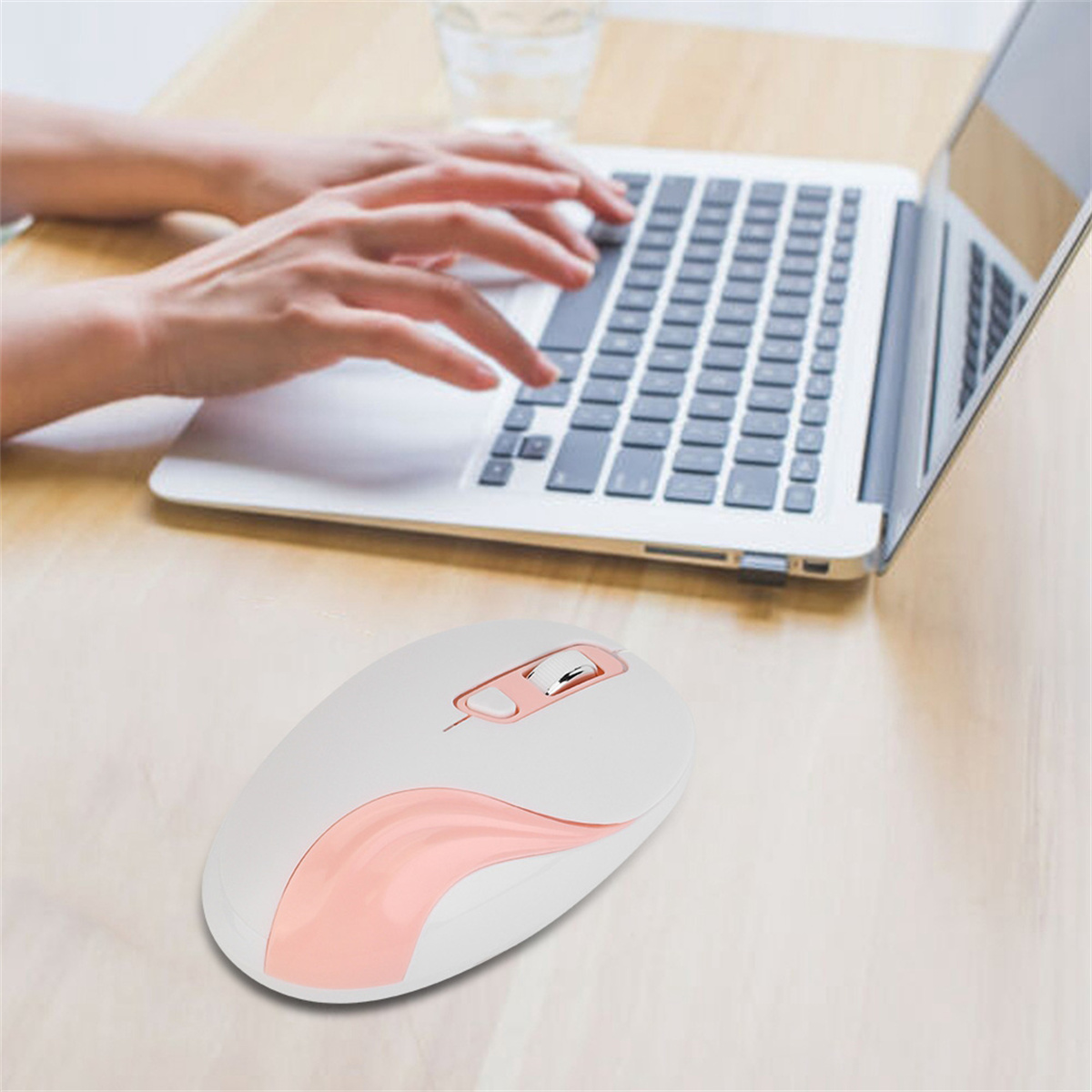 Hände auf einer Laptop-Tastatur, eine weiße und rosa Maus auf einem Holztisch.