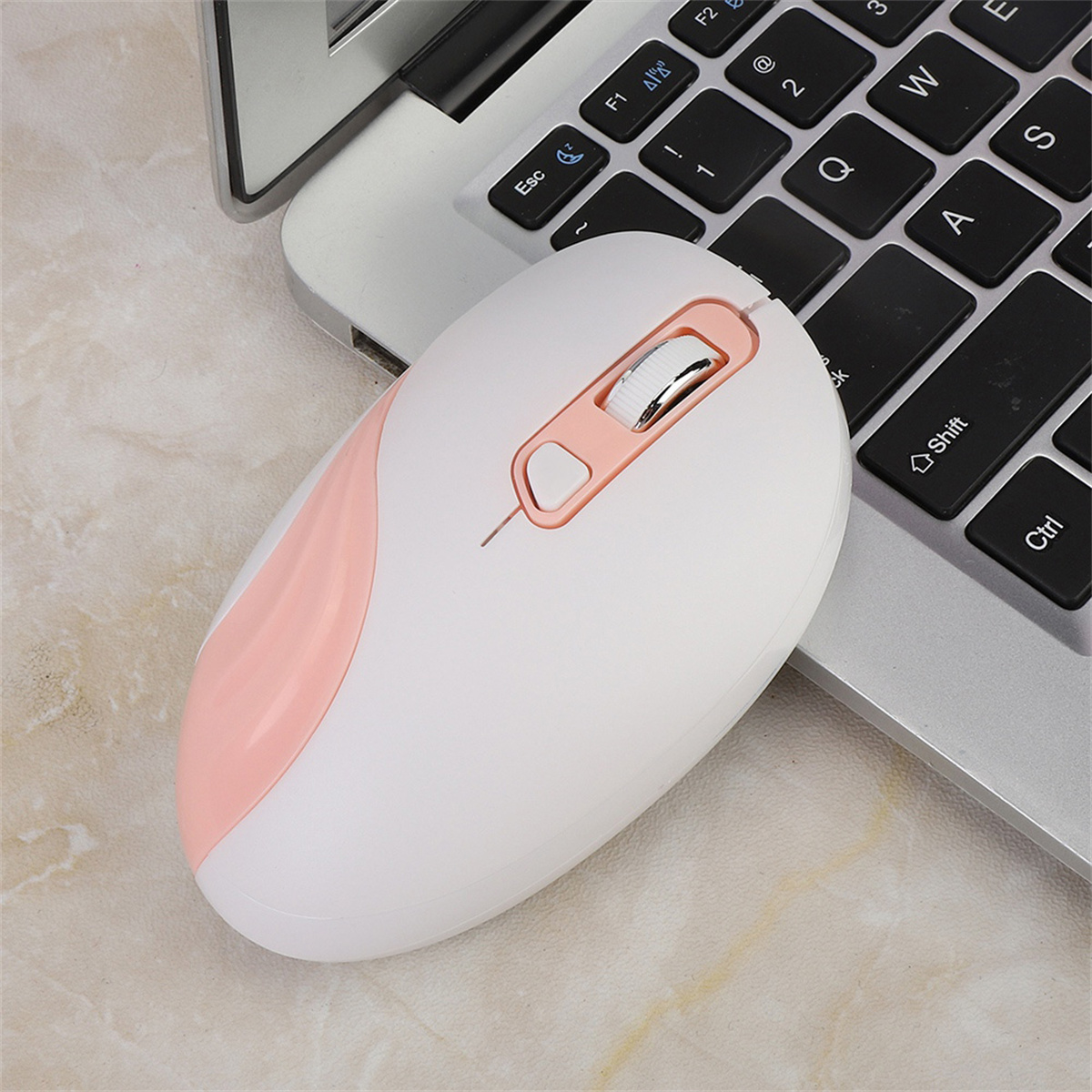 Weiße und rosa kabellose Maus auf einer silbernen Laptop-Tastatur, Draufsicht, rechts abgewinkelt.