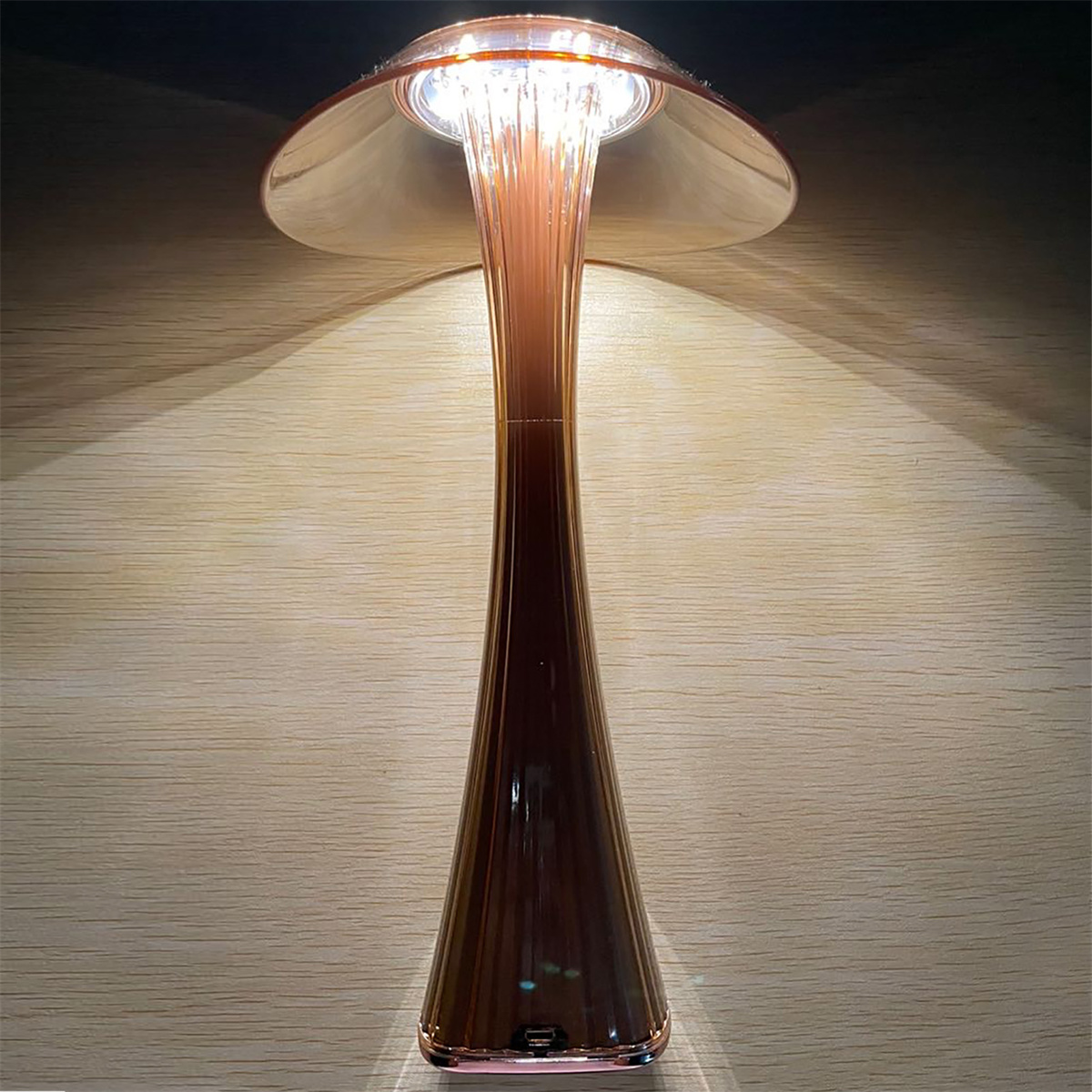 Eine Tischlampe mit goldfarbenem Stiel und pilzförmigem Kopf, die warmes Licht wirft.