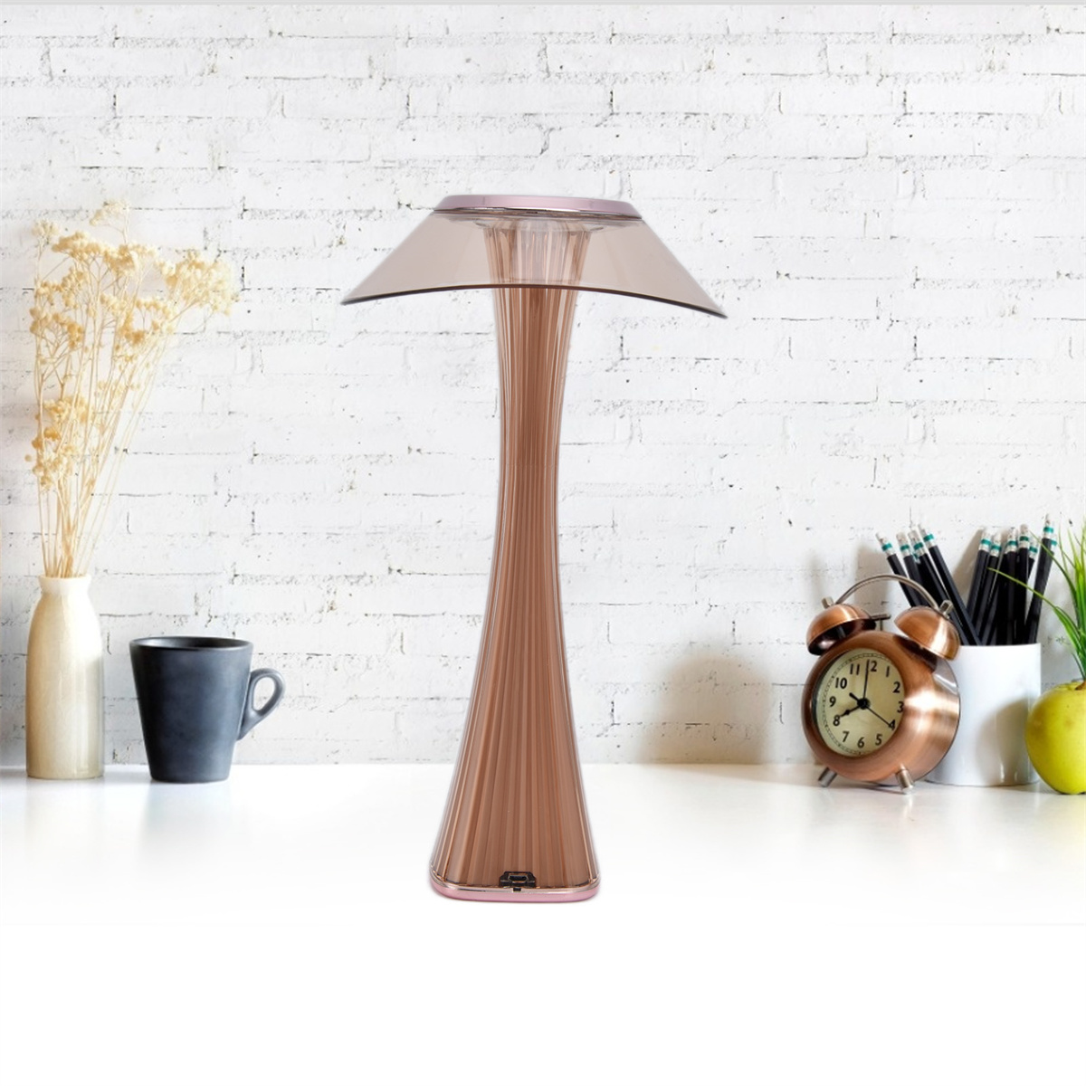 Rosa Lampe mit Schirm auf einem weißen Tisch. Wecker und Tasse stehen auf dem Tisch.