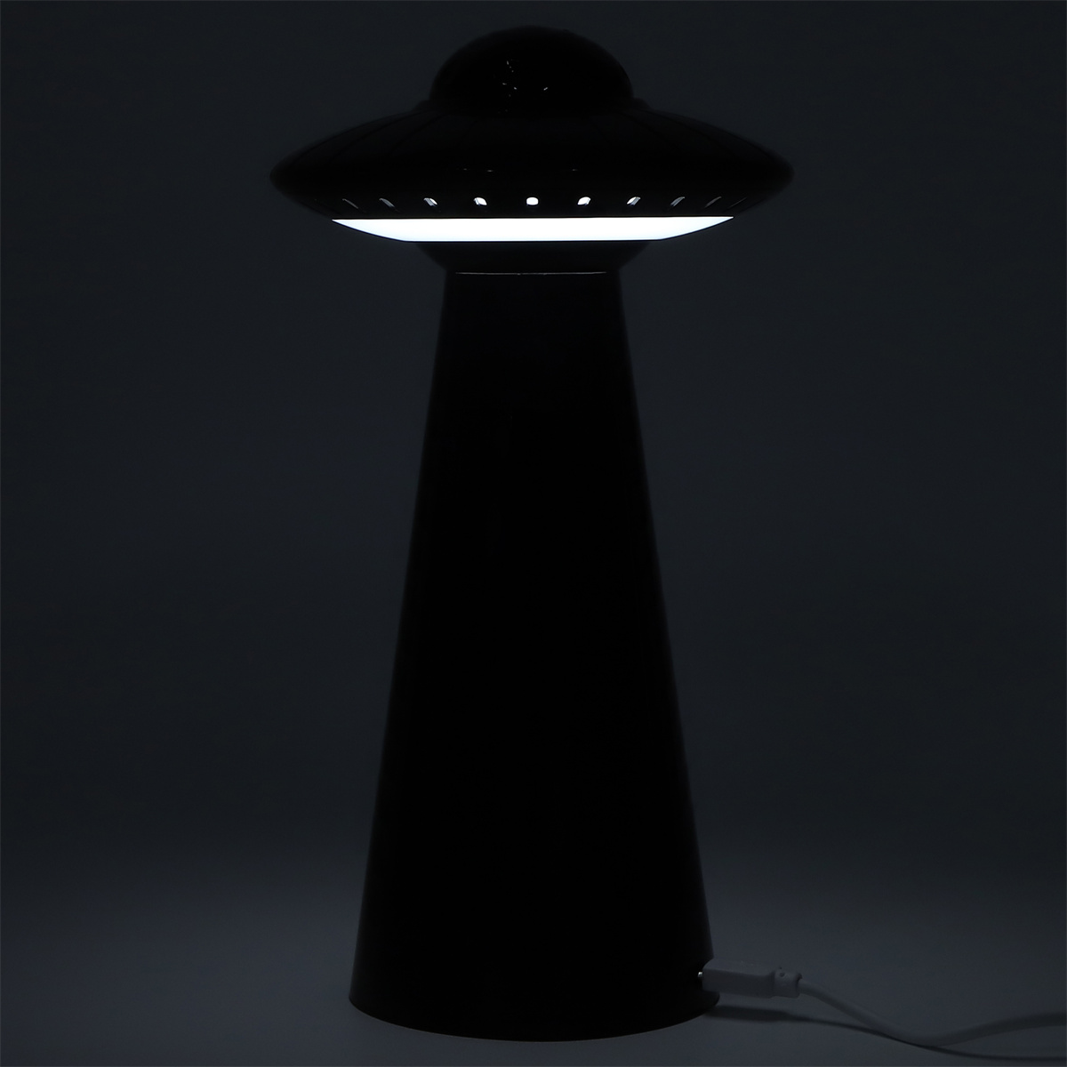 Schwarze UFO-förmige Lampe mit hellem weißen Licht. Sie hat einen hohen, konischen Sockel und befindet sich auf dunklem Hintergrund.