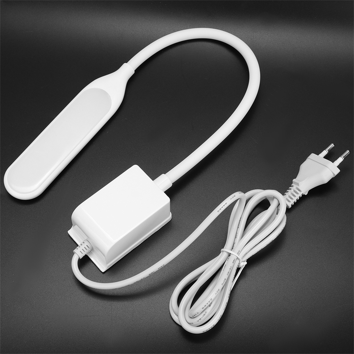 Weiße, biegsame Schreibtischlampe mit Netzteil und Kabel auf schwarzer Oberfläche. Das Kabel ist ordentlich aufgerollt.