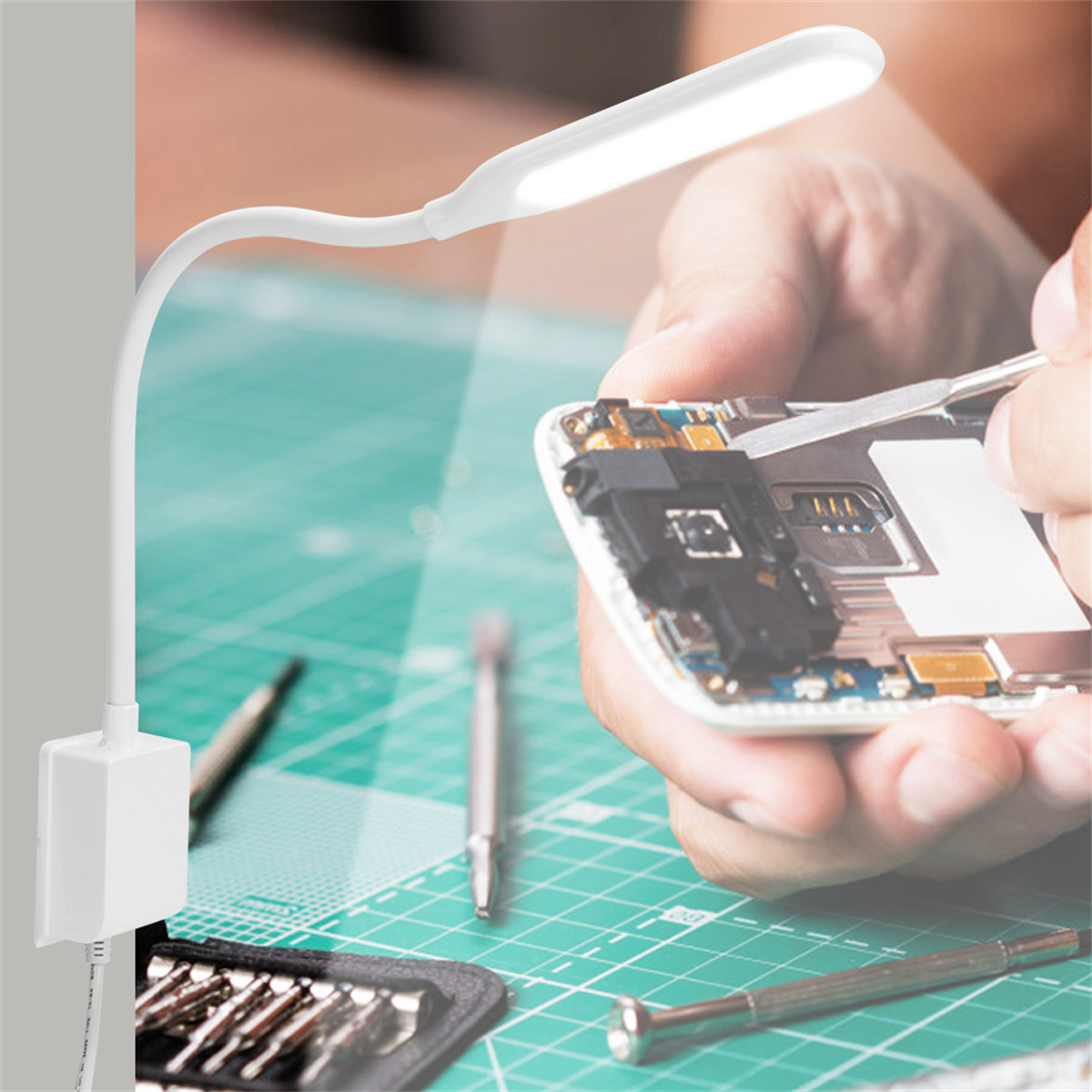 Weiße Schreibtischlampe mit repariertem Telefon und Werkzeugen. Grüne Schneidematte.