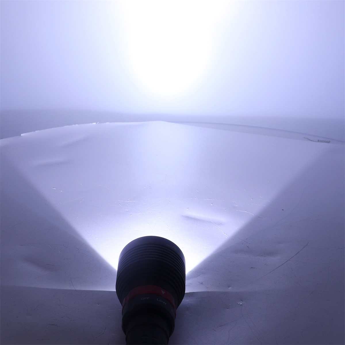 Taschenlampe, die helles weißes Licht auf eine Oberfläche mit leichtem Lilastich abstrahlt.
