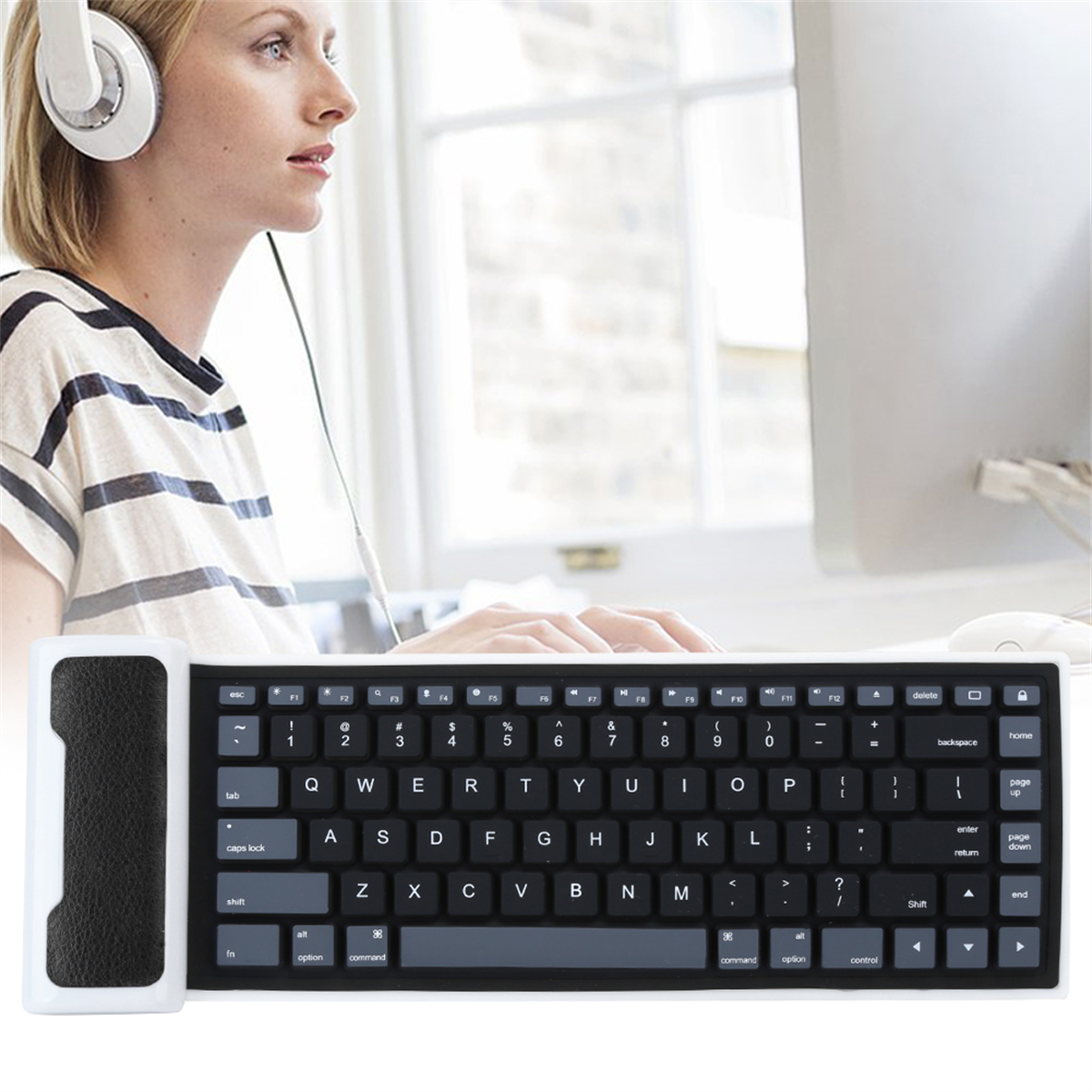 Eine Frau mit Kopfhörern benutzt eine Tastatur neben einem Computerbildschirm, neben einer Tastaturabdeckung.