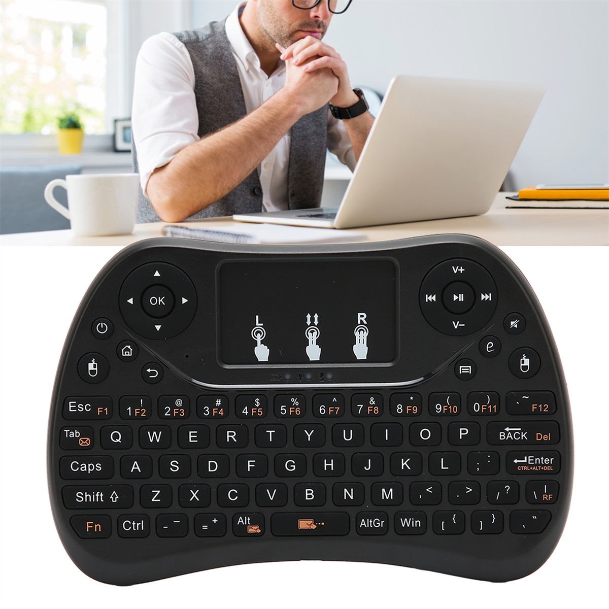 Schwarze Mini-Tastatur mit Touchpad, im Hintergrund arbeitet ein Mann an einem Laptop.