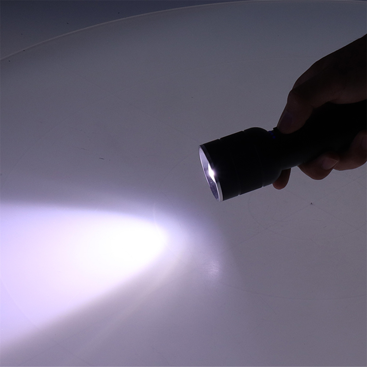 Eine Hand leuchtet mit einer schwarzen Taschenlampe und beleuchtet eine weiße Oberfläche. Das helle Licht kontrastiert.