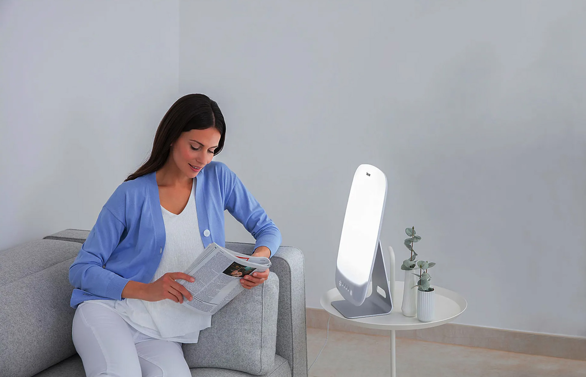 Frau liest in der Nähe einer hellen weißen Lichttherapielampe.