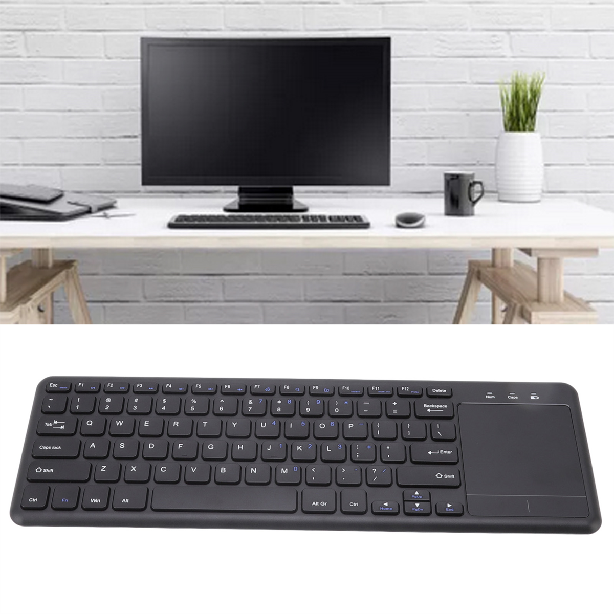 Eine schwarze Tastatur mit Touchpad auf einem Schreibtisch mit Computermonitor im Hintergrund.