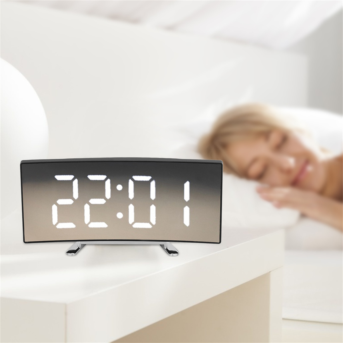Digitaler Wecker mit der Anzeige 22:01. Frau schläft im Hintergrund. Weißer Tisch und Hintergrund.