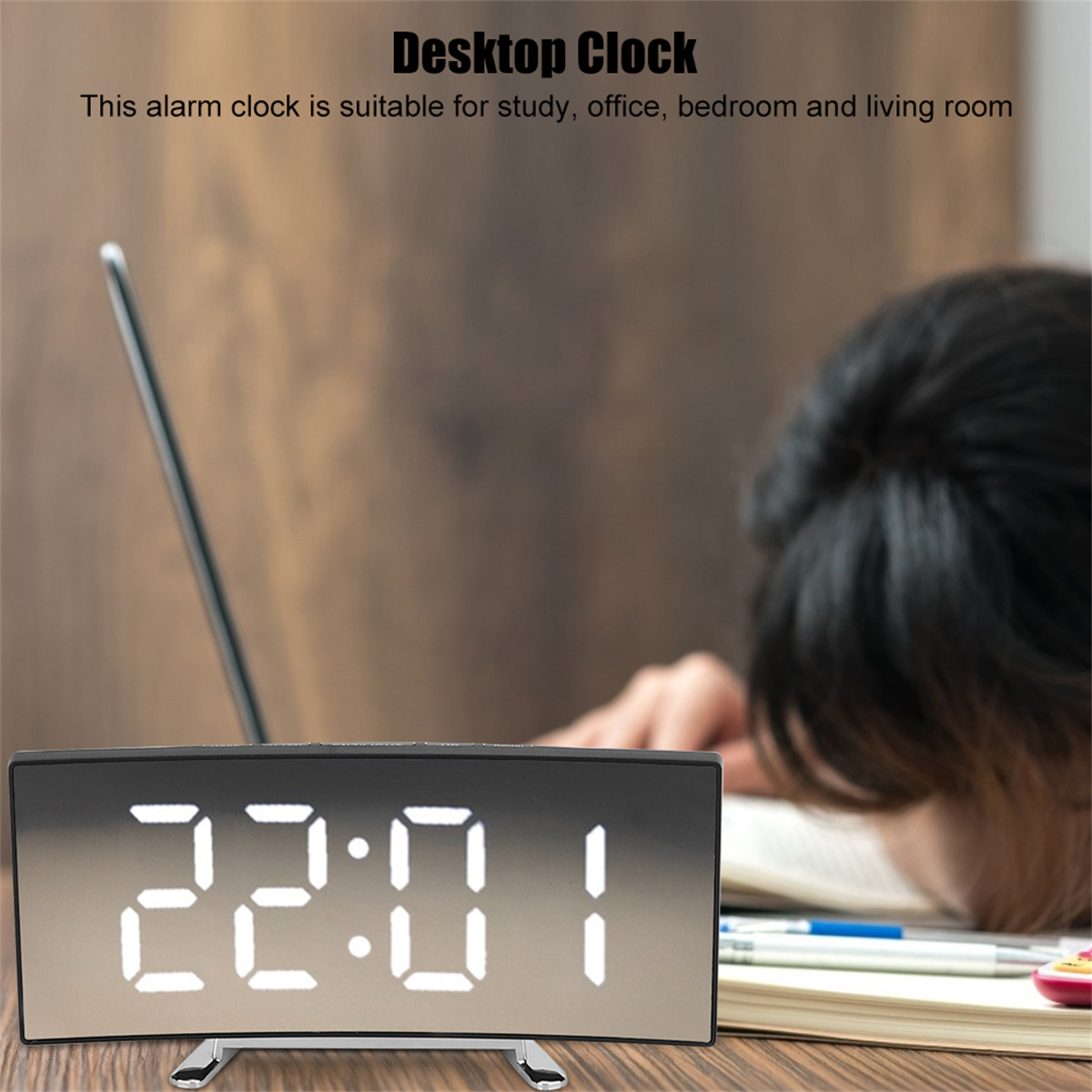 Digitaluhr mit der Anzeige 22:01. Die Uhr steht auf einem Schreibtisch, im Hintergrund eine verschwommene Person.