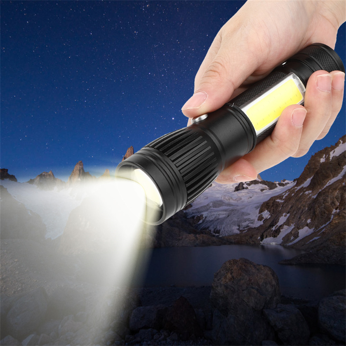 Hand, die eine schwarze Taschenlampe hält, die nachts Licht über einen See und schneebedeckte Berge scheint.