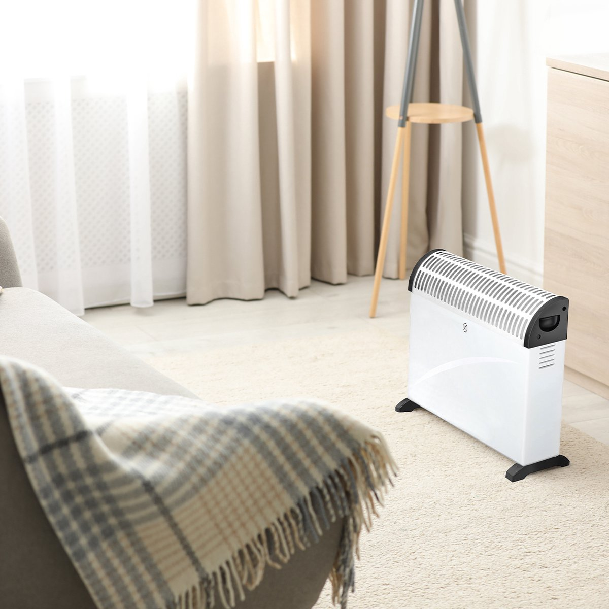 Een witte elektrische kachel staat op een kleed, in een lichte kamer. Een deken ligt over een stoel.