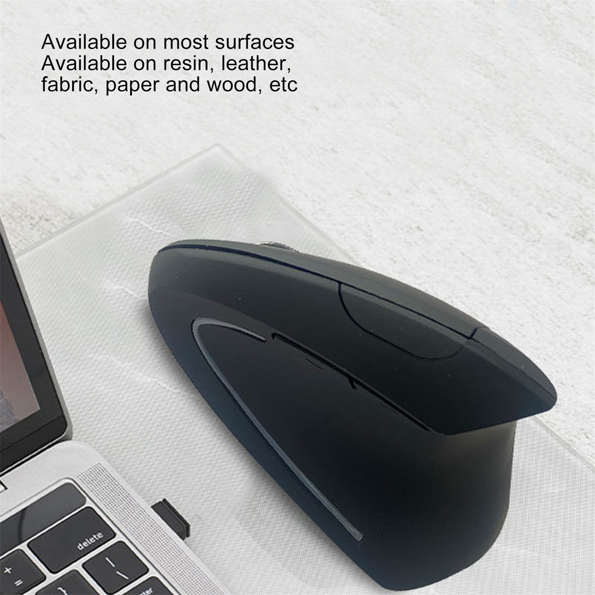 Eine schwarze ergonomische Maus auf einer weißen Oberfläche neben einem Laptop, mit Text.