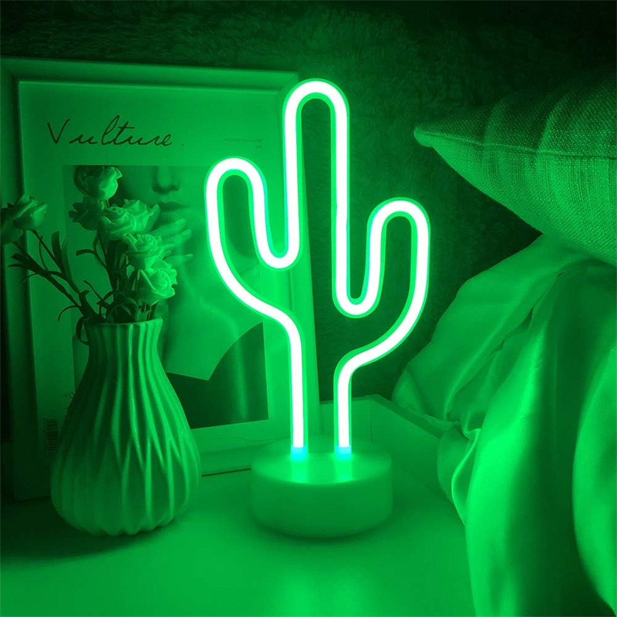 Grüne Neon-Kaktuslampe auf einem Tisch mit Vase und Magazin.