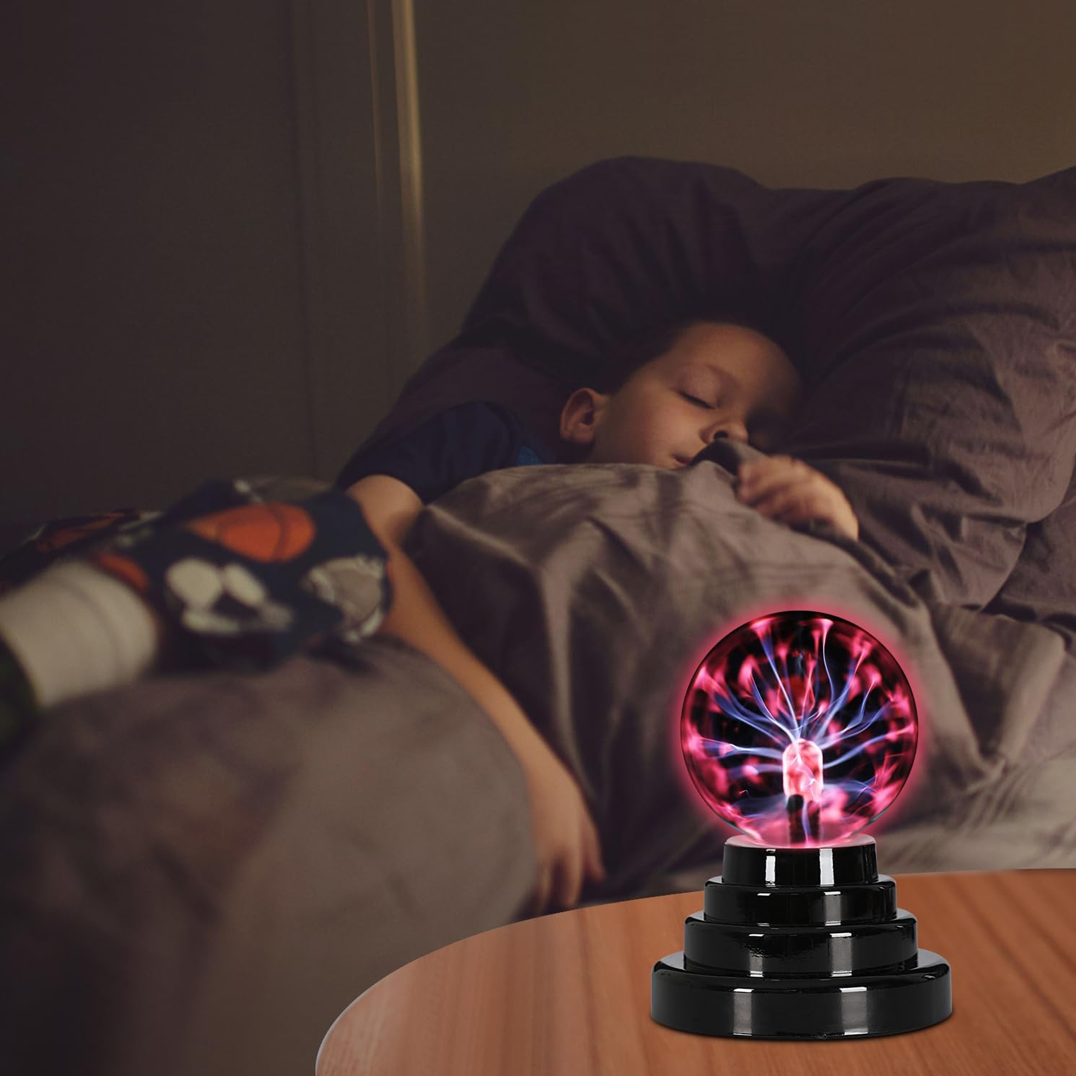 Ein Kind schläft im Bett. Eine Plasmakugel auf einem Tisch leuchtet in seiner Nähe mit roten und blauen Lichtern.